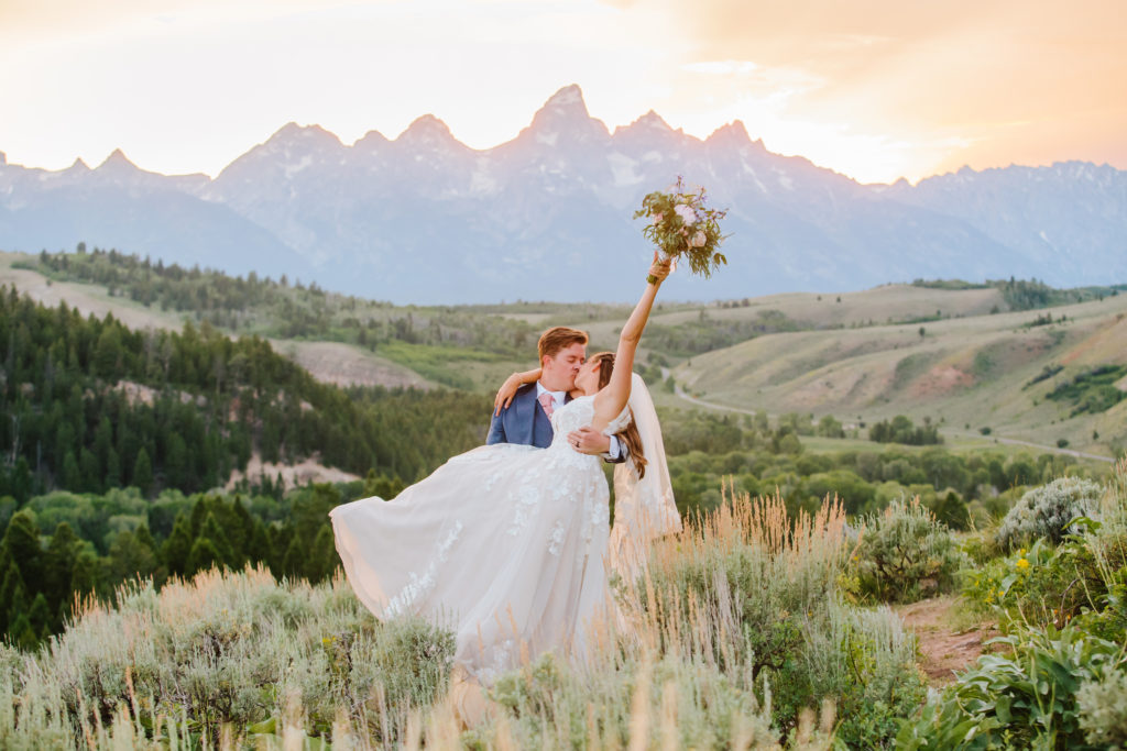 Bride raises flowers in celebration while she kisses her husband at jackson hole wedding
