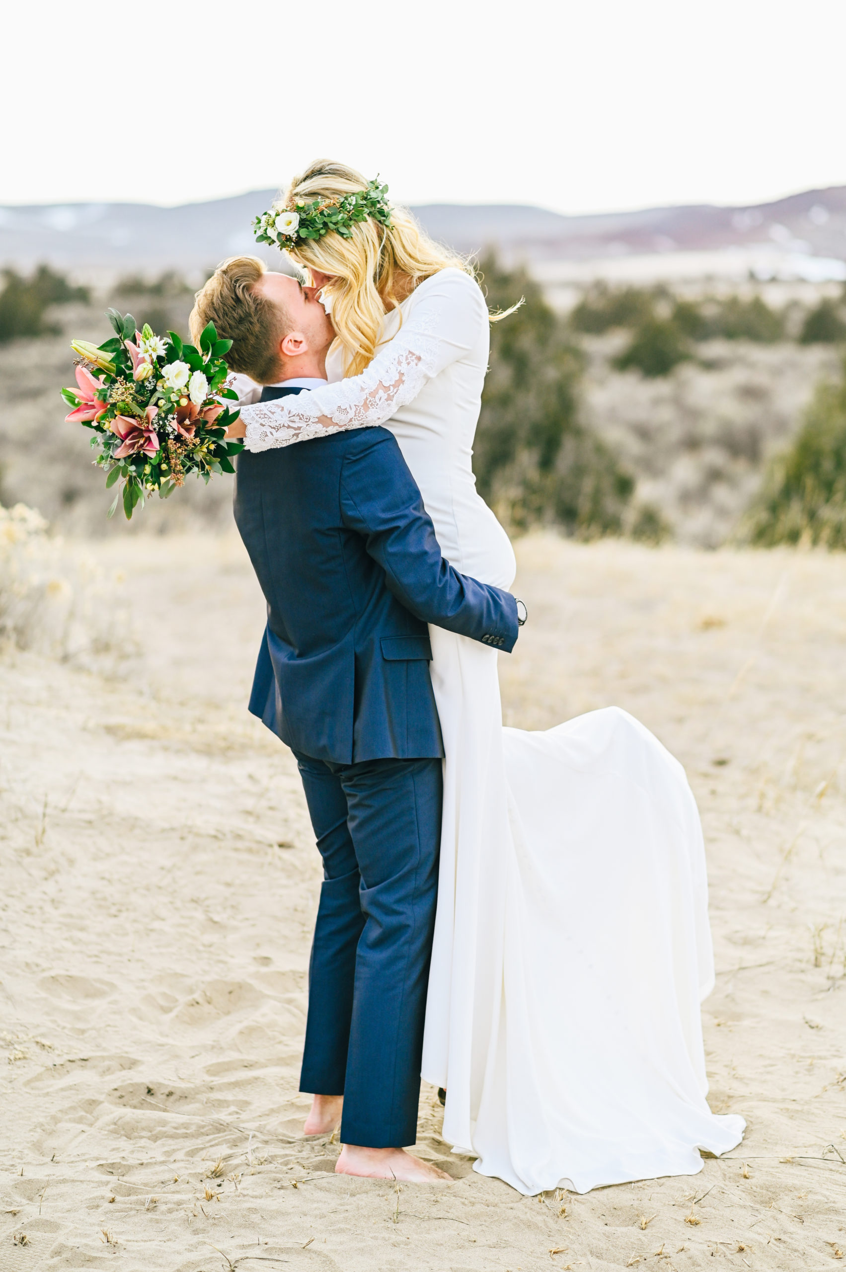 groom lifting bride up and kissing her in the sane dunes