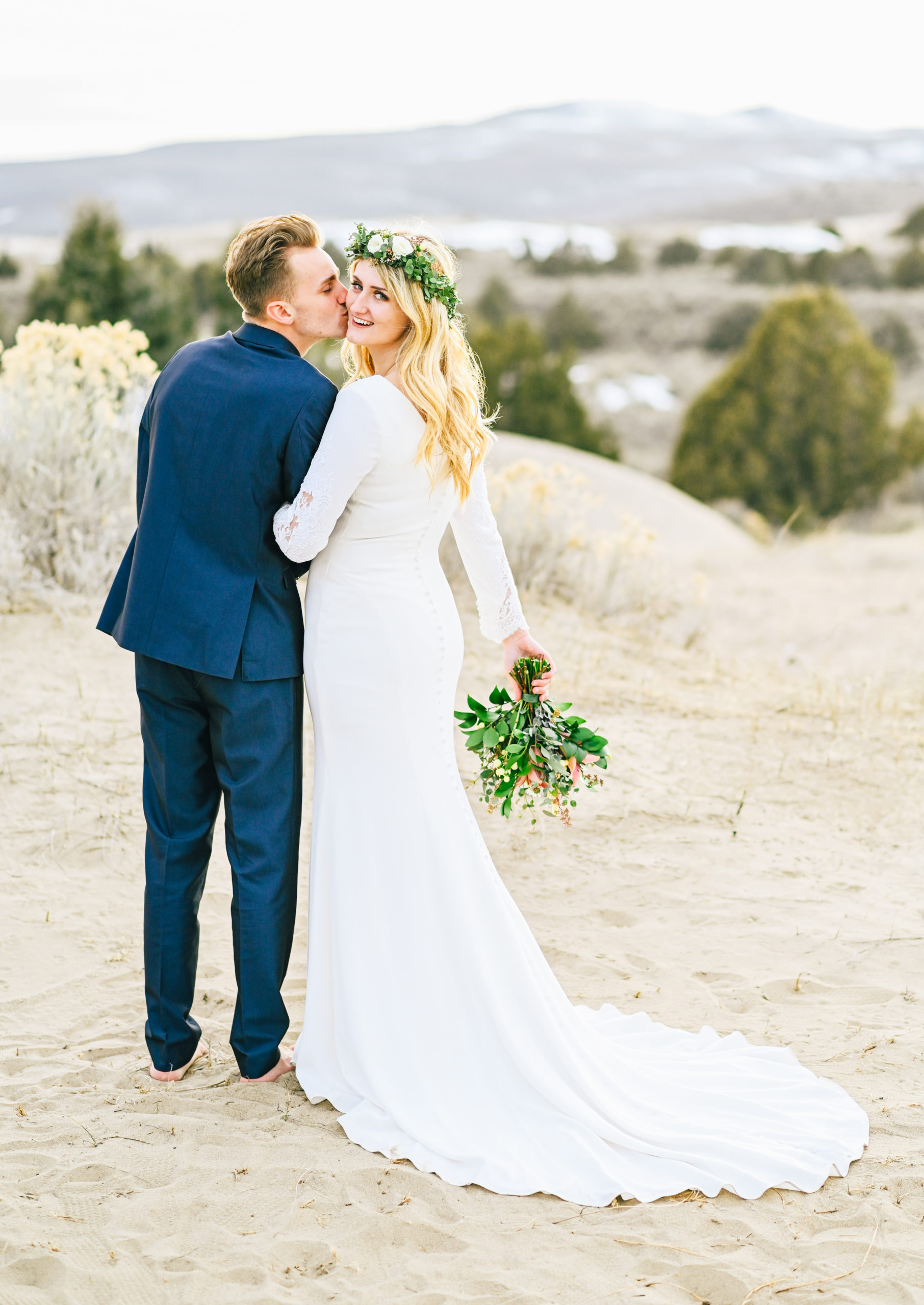 Bride and groom walking away while bride looks over her shoulder and smiles at camera at sand dunes in idaho 