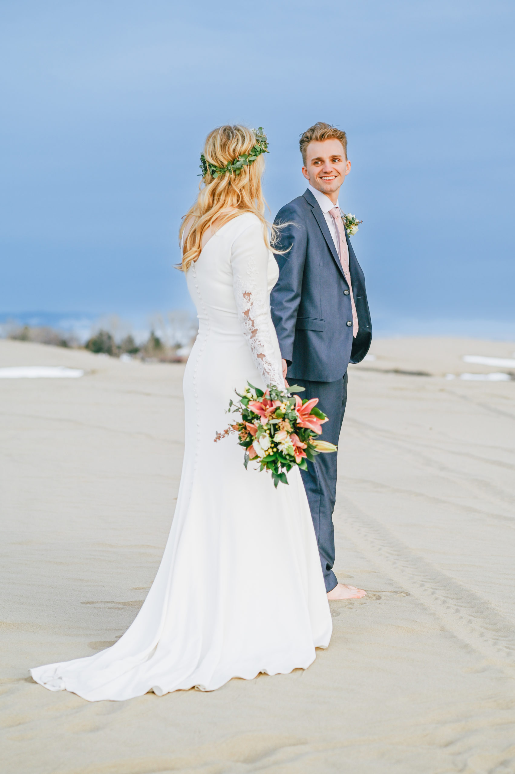 groom holding hand and leading bride into sandy beach