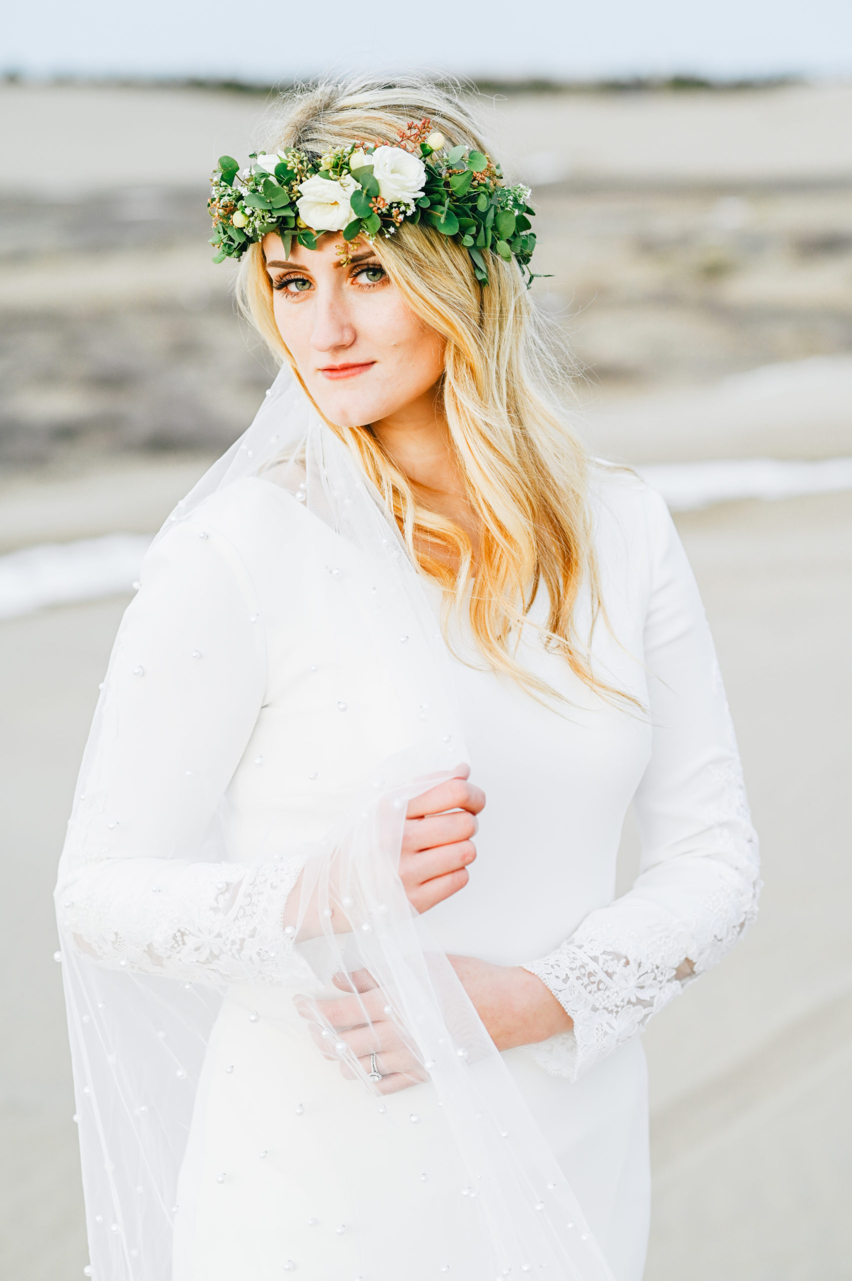 beautiful rigby idaho bride at sand dunes grabing veil and she gazes into the camera wearing a green and white floral crown