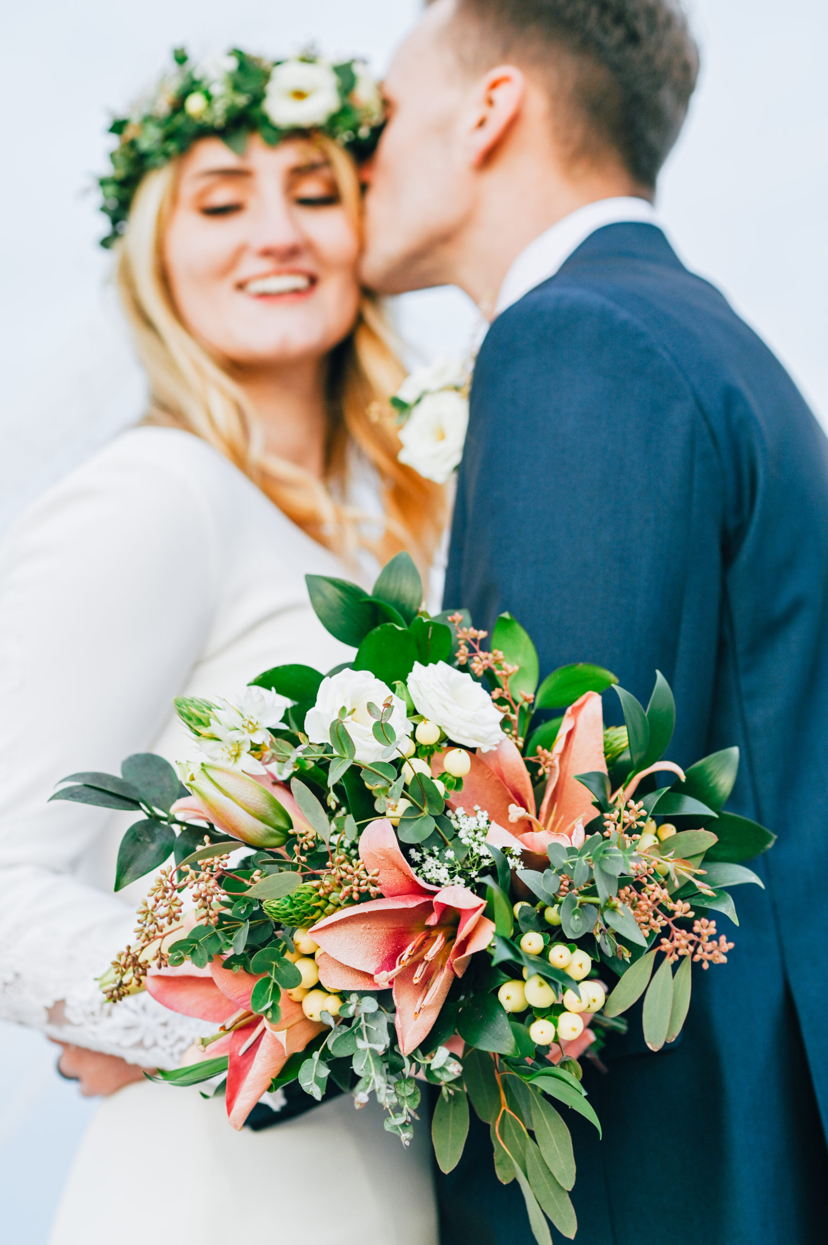 close up of bouquet while groom kisses bride