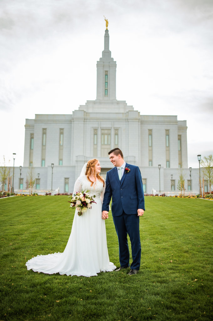 bride and groom wearing bridal clothes holding hands in front of pocatello temple