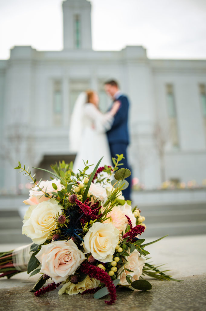 bridal bouquet of white and red roses on ground with bridal couple behind them