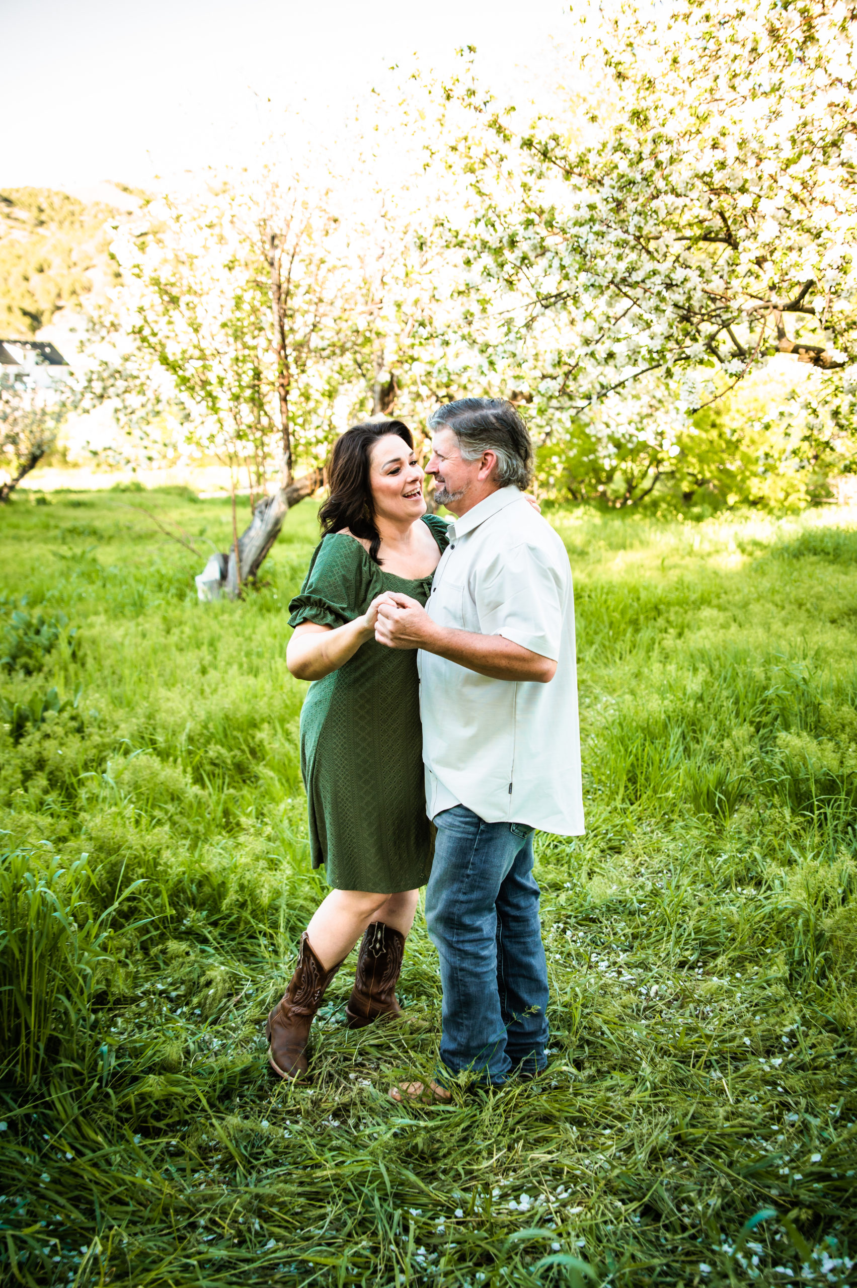 woman wearing green dress dancing in a grassy field with man wearing button down shirt, jeans and boots during Western Sunset Engagements
