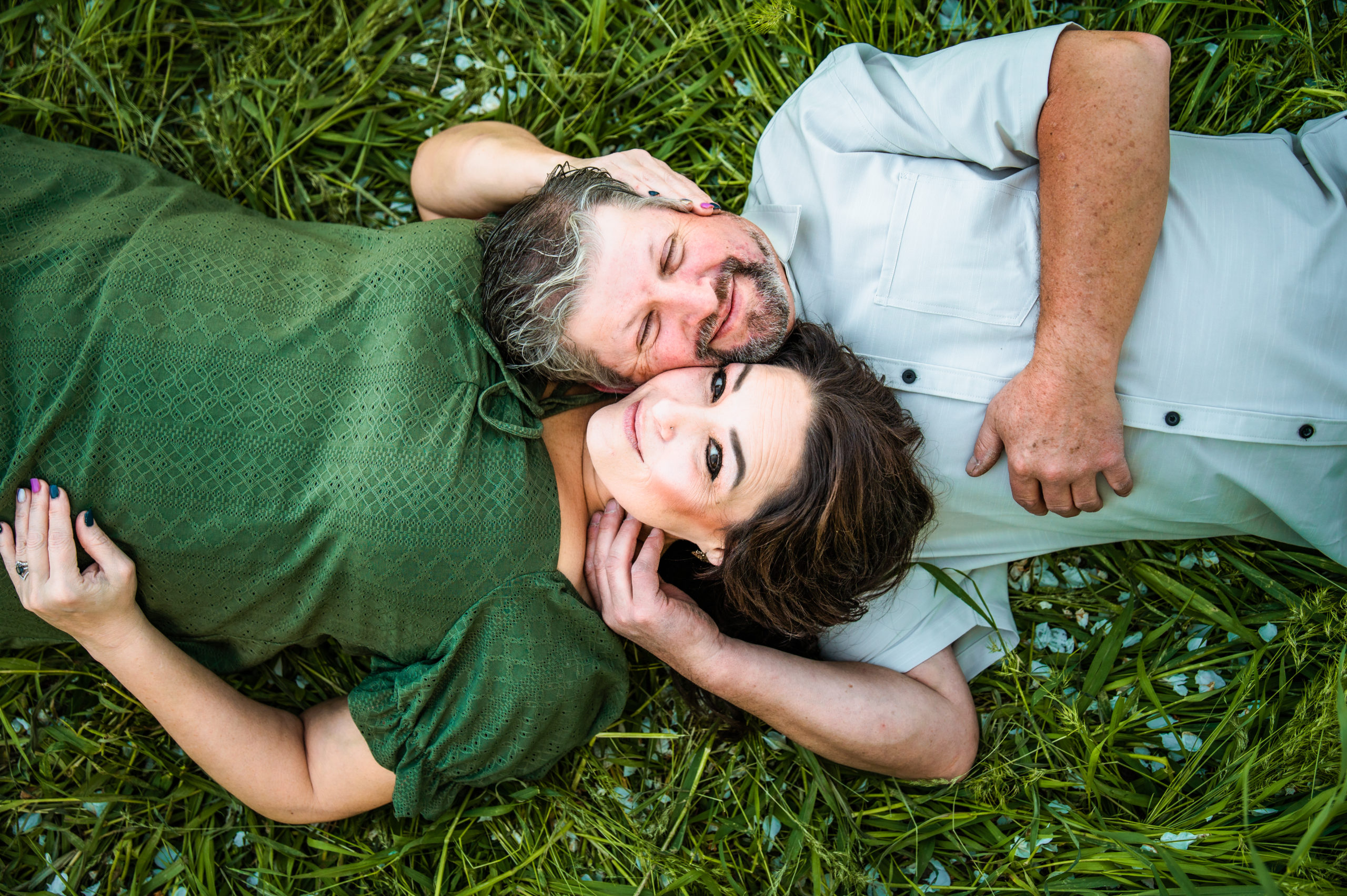 engaged couple laying in grass touching heads talking during outdoor engagements
