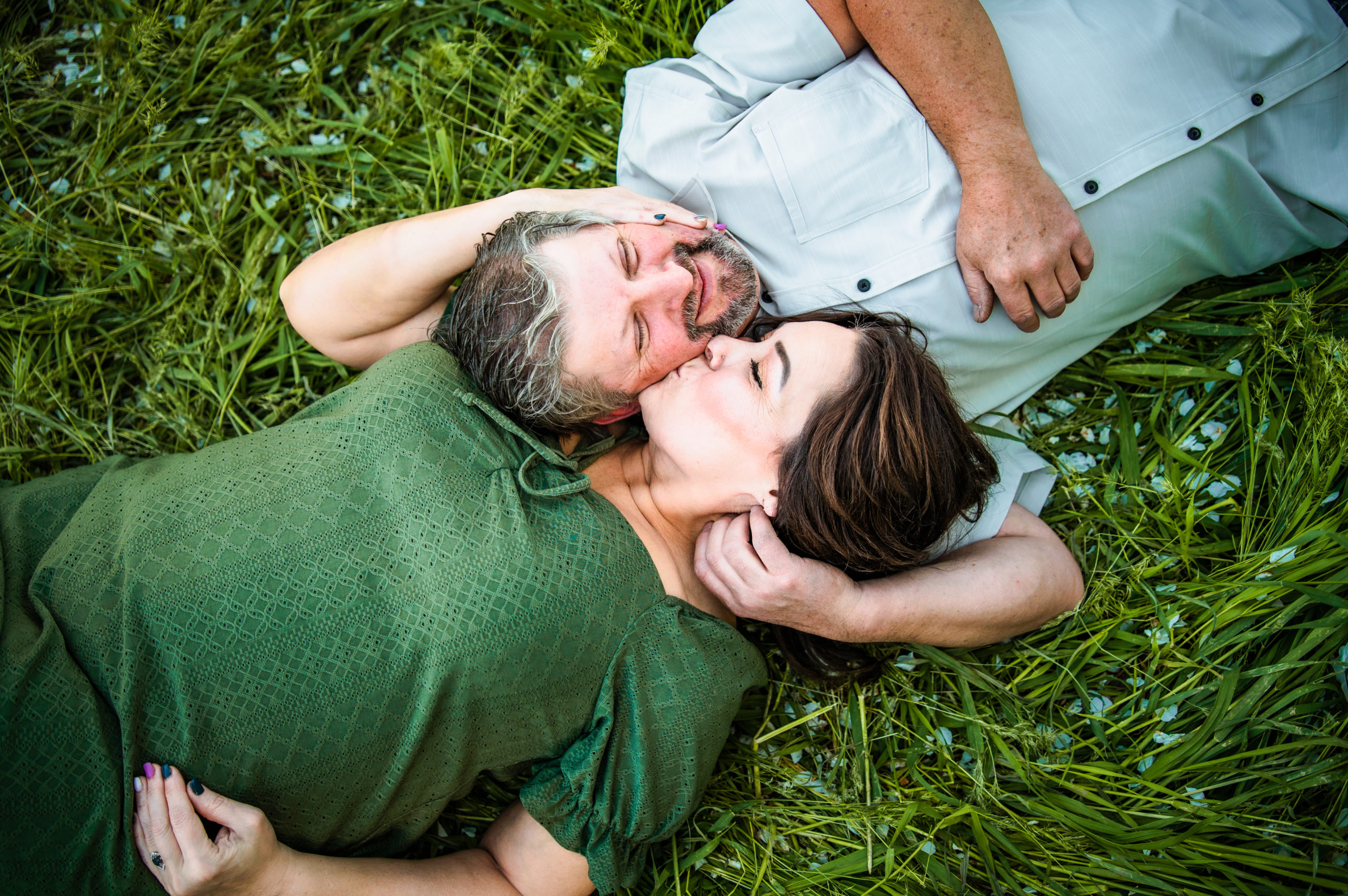 man and woman laying in grass while woman kisses man's cheek during engagements