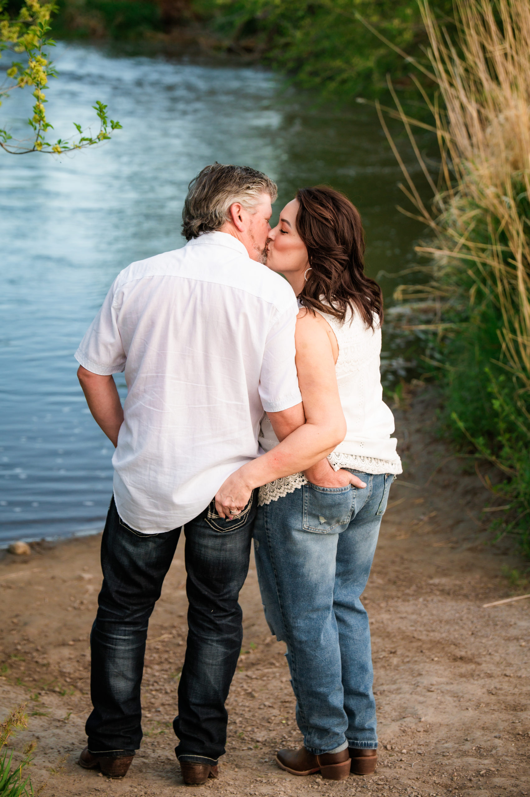 engaged couple with hands in one another's back pockets kissing
