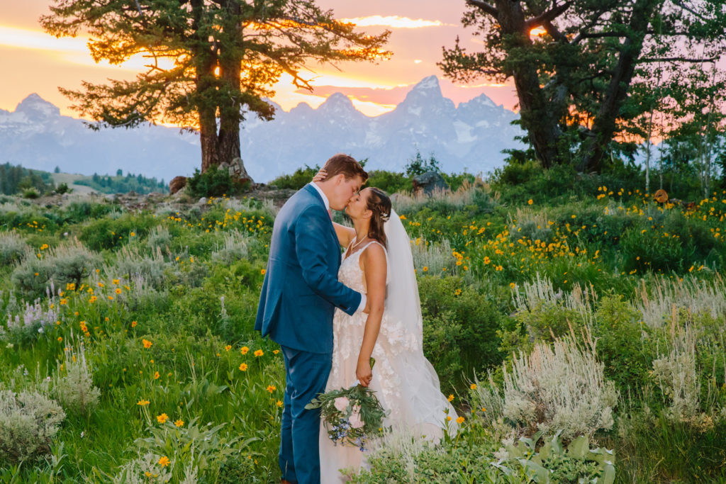 couple kisses with sunset at wedding tree and tetons at jackson hole behind them