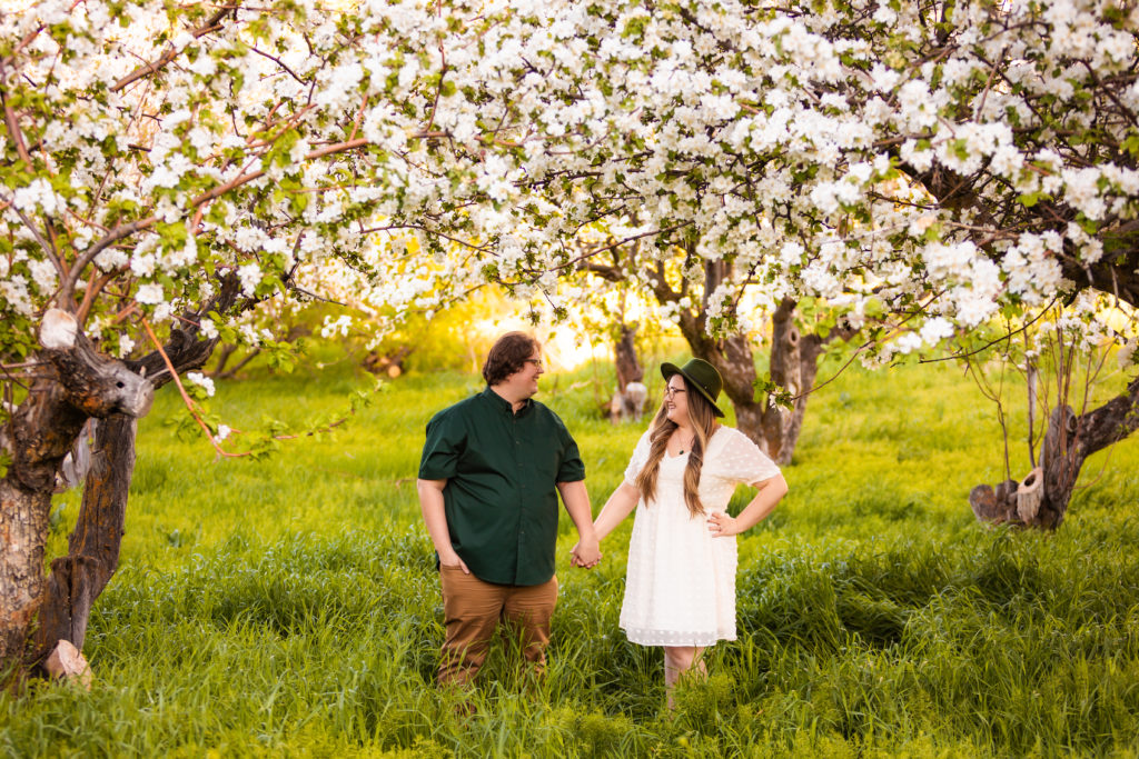 engaged couple holding hands in apple blossoms during engagement session