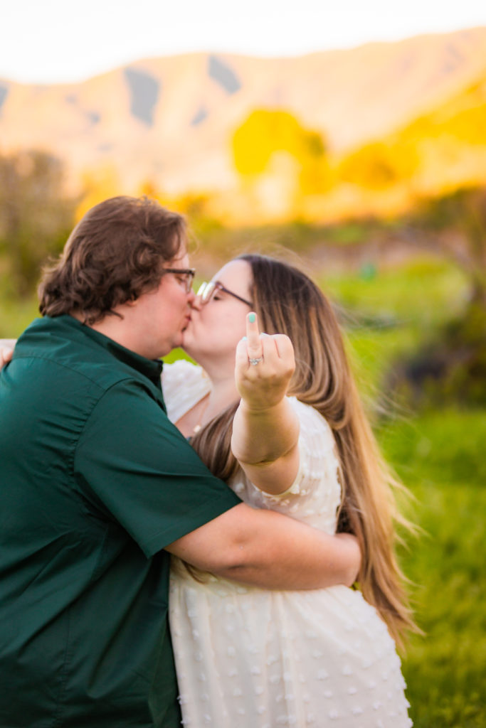woman kissing fiance while holding up ring finger
