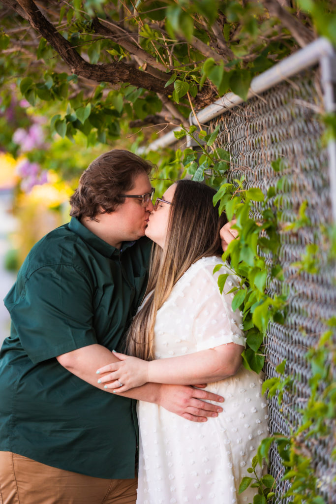 man kissing woman against fence during outdoor engagement session