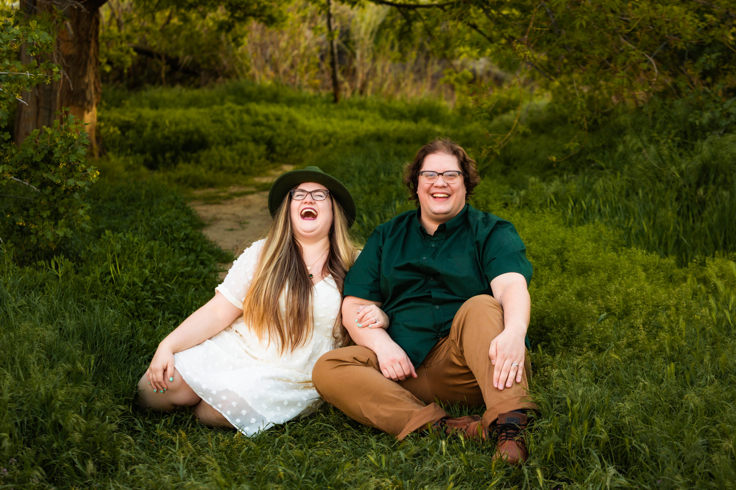 newly engaged couple sitting in grass laughing together