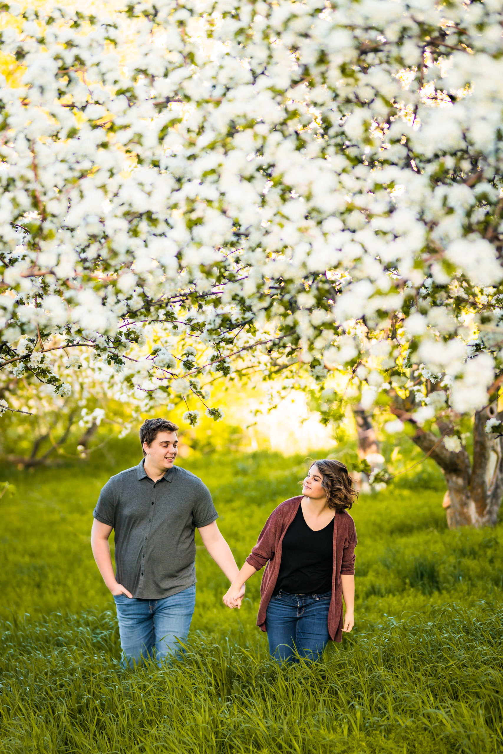 man and woman walking in apple blossoms during engagement session