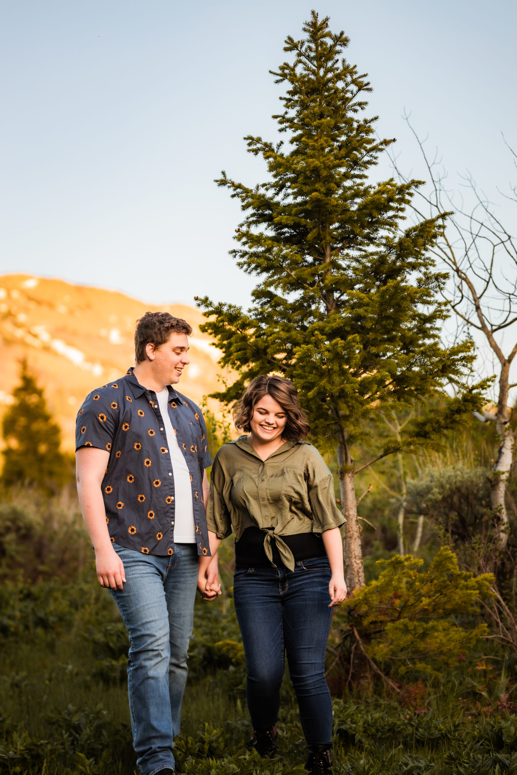 couple walking through forest holding hands during Sunflower Pocatello Engagements