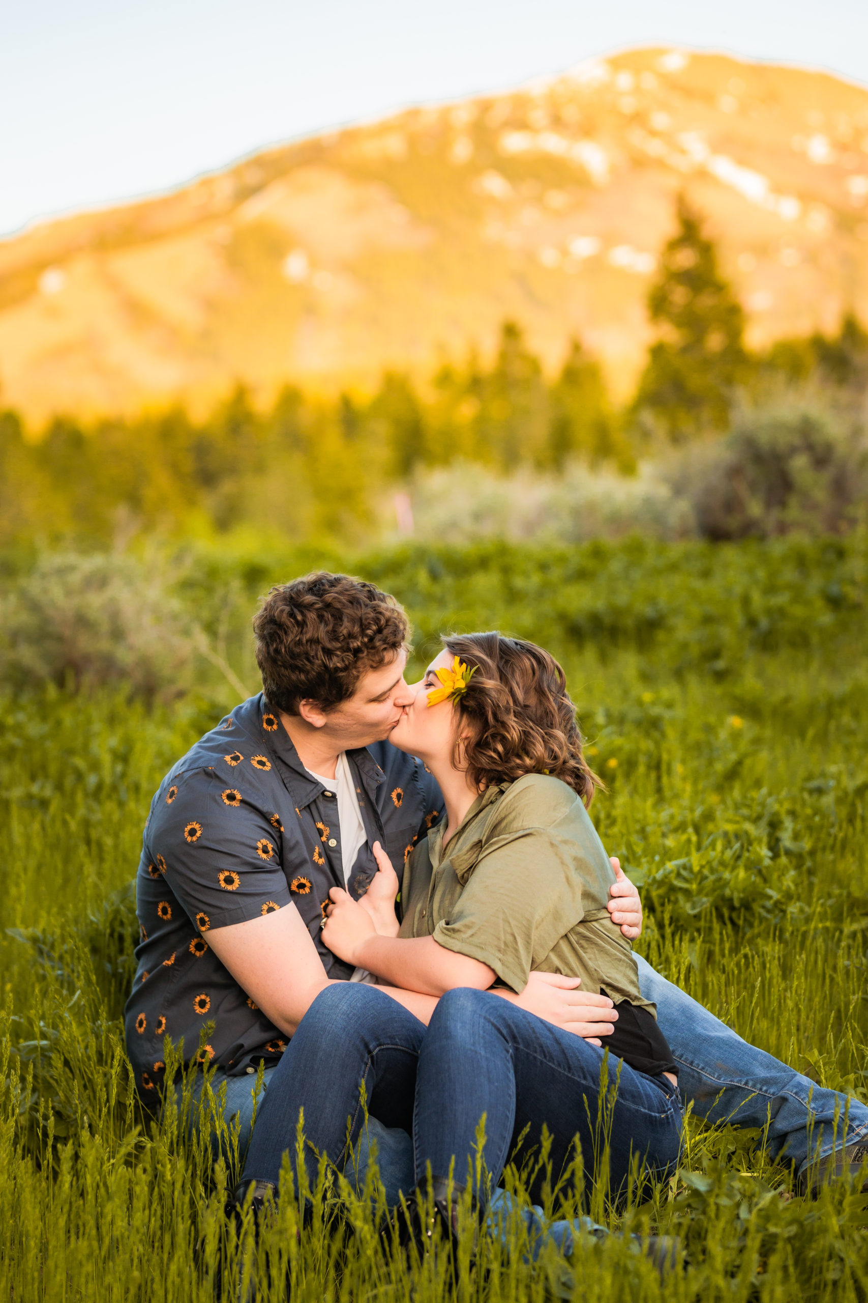 couple sitting in grass kissing during spring outdoor engagements