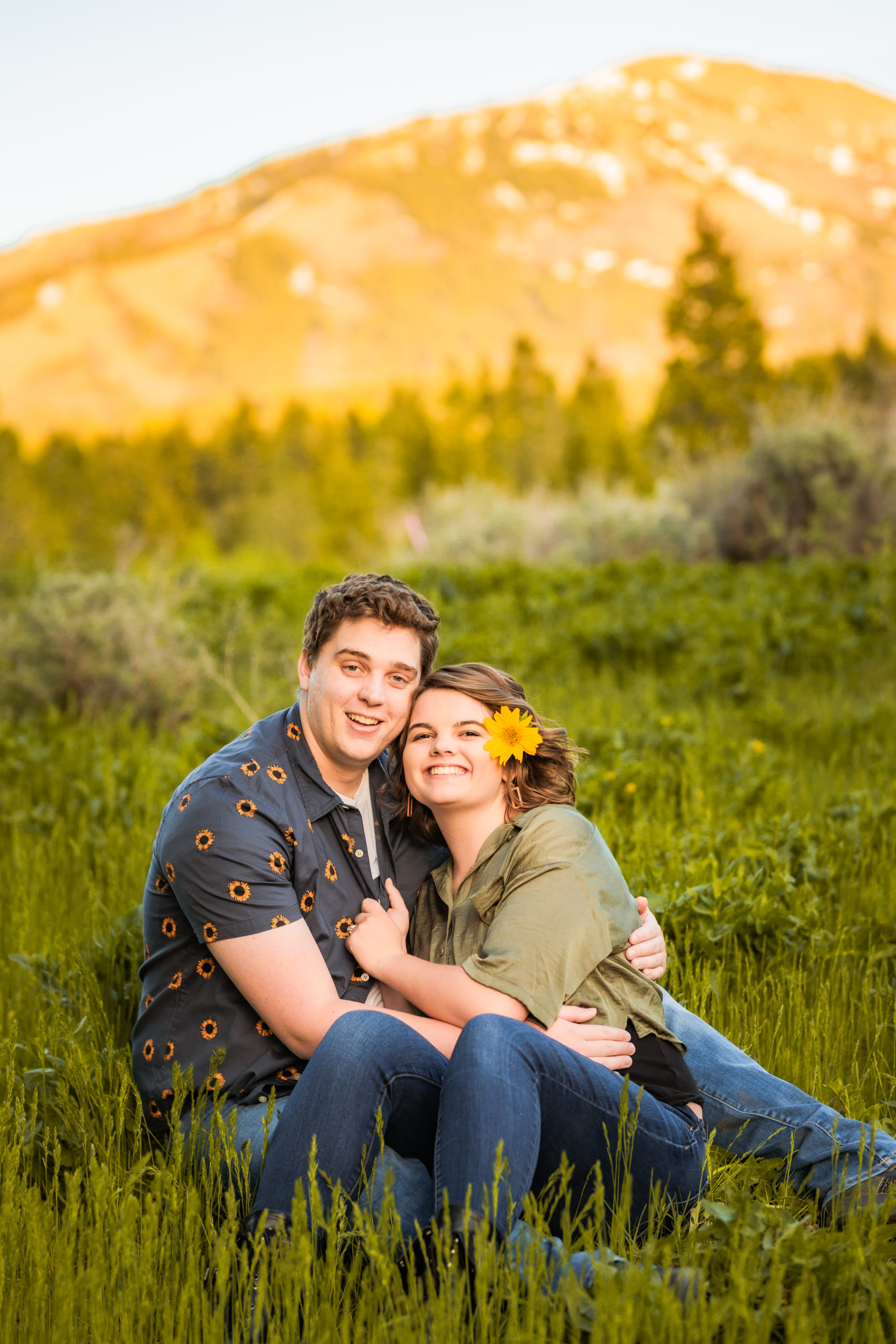 newly engaged couple sitting together in field embracing during Sunflower Pocatello Engagements