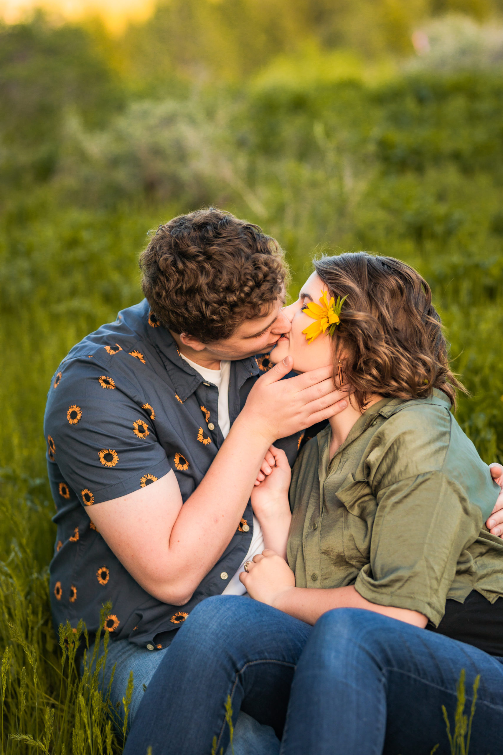 couple sitting in field kissing during engagements