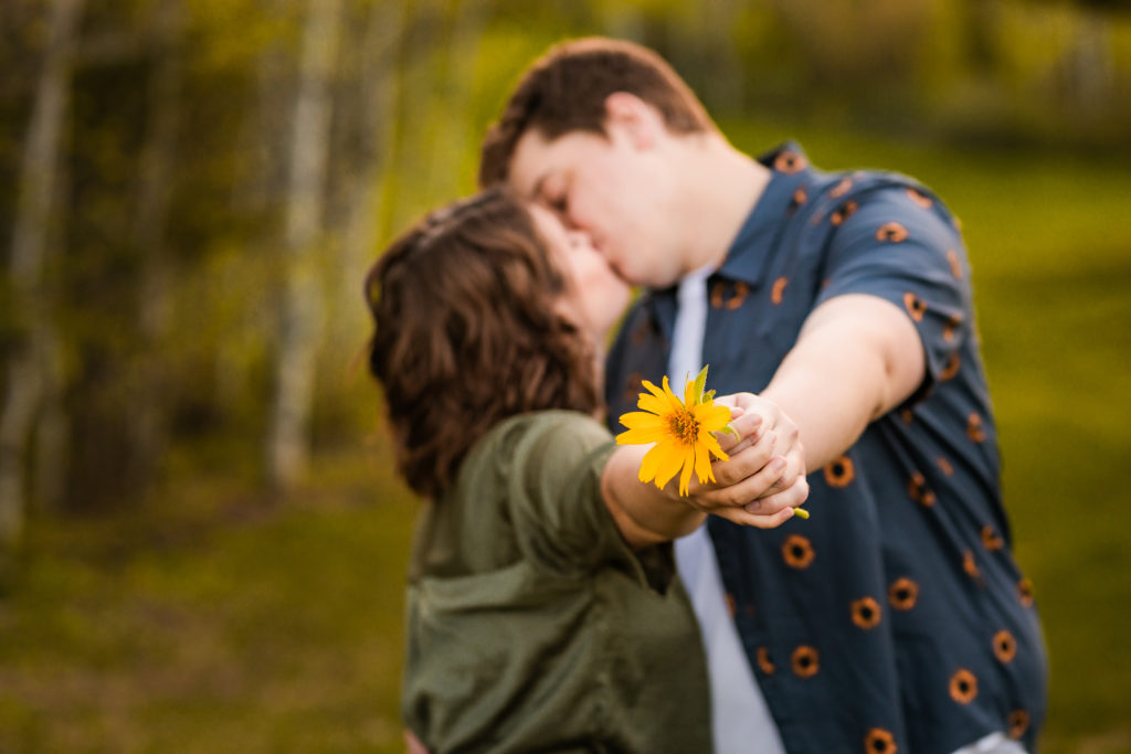 newly engaged couple kissing while holding yellow flower 