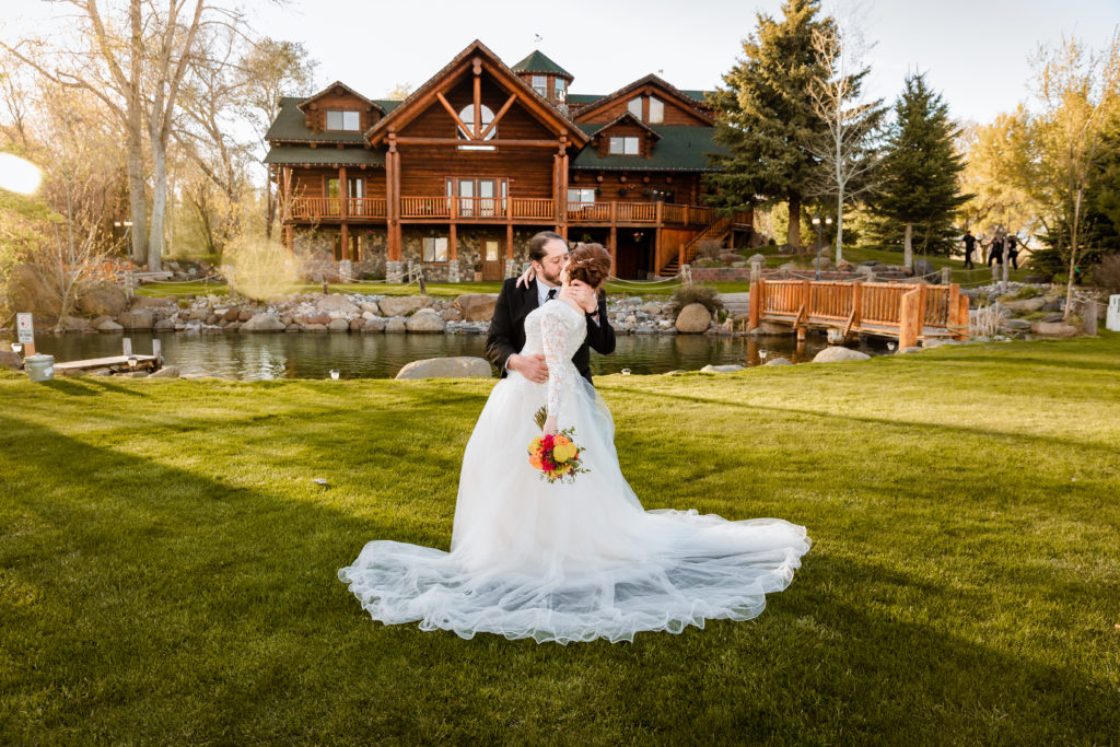 groom dips his bride back as he kisses her in front of the cabin wedding venue in Rigby Idaho