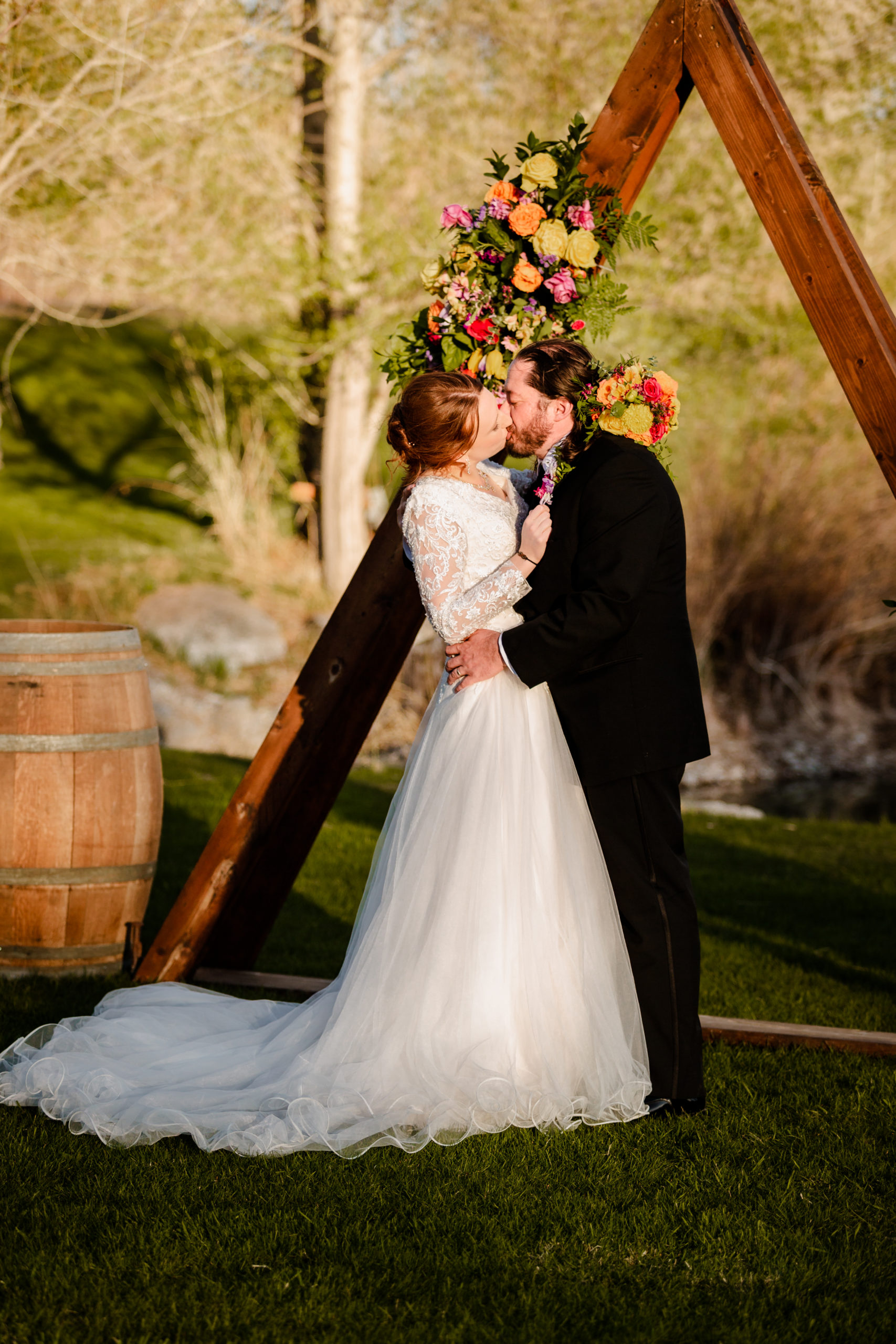 outdoor wedding ceremony at LaBelle Lake wedding venue with bride and groom sharing a kiss under their triangle wedding arch decorated in orange florals