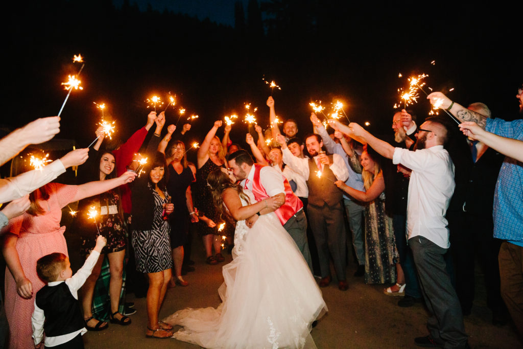 groom kissing bride as he dips her back with their guests surrounding them with sparklers for their grand wedding exit