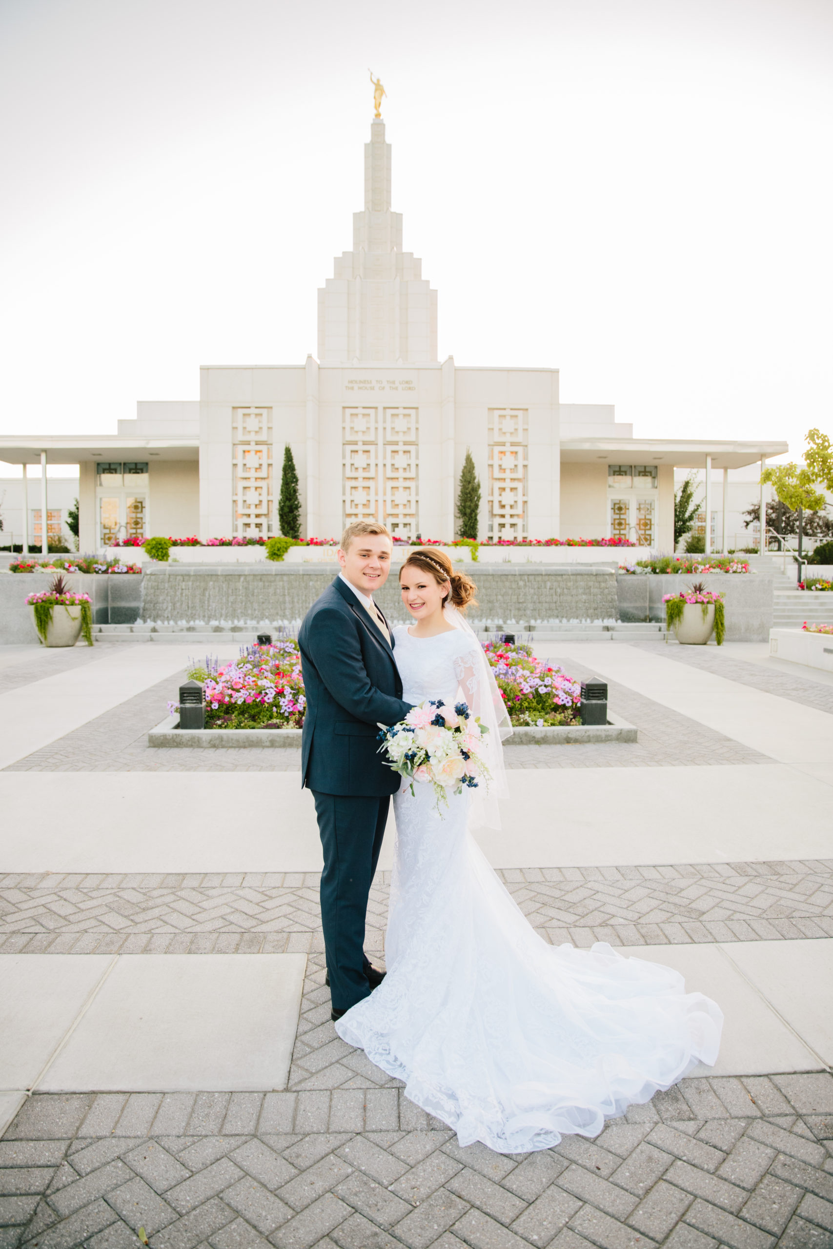 bride and groom standing outside of Idaho Falls temple in front of flowers at golden hour