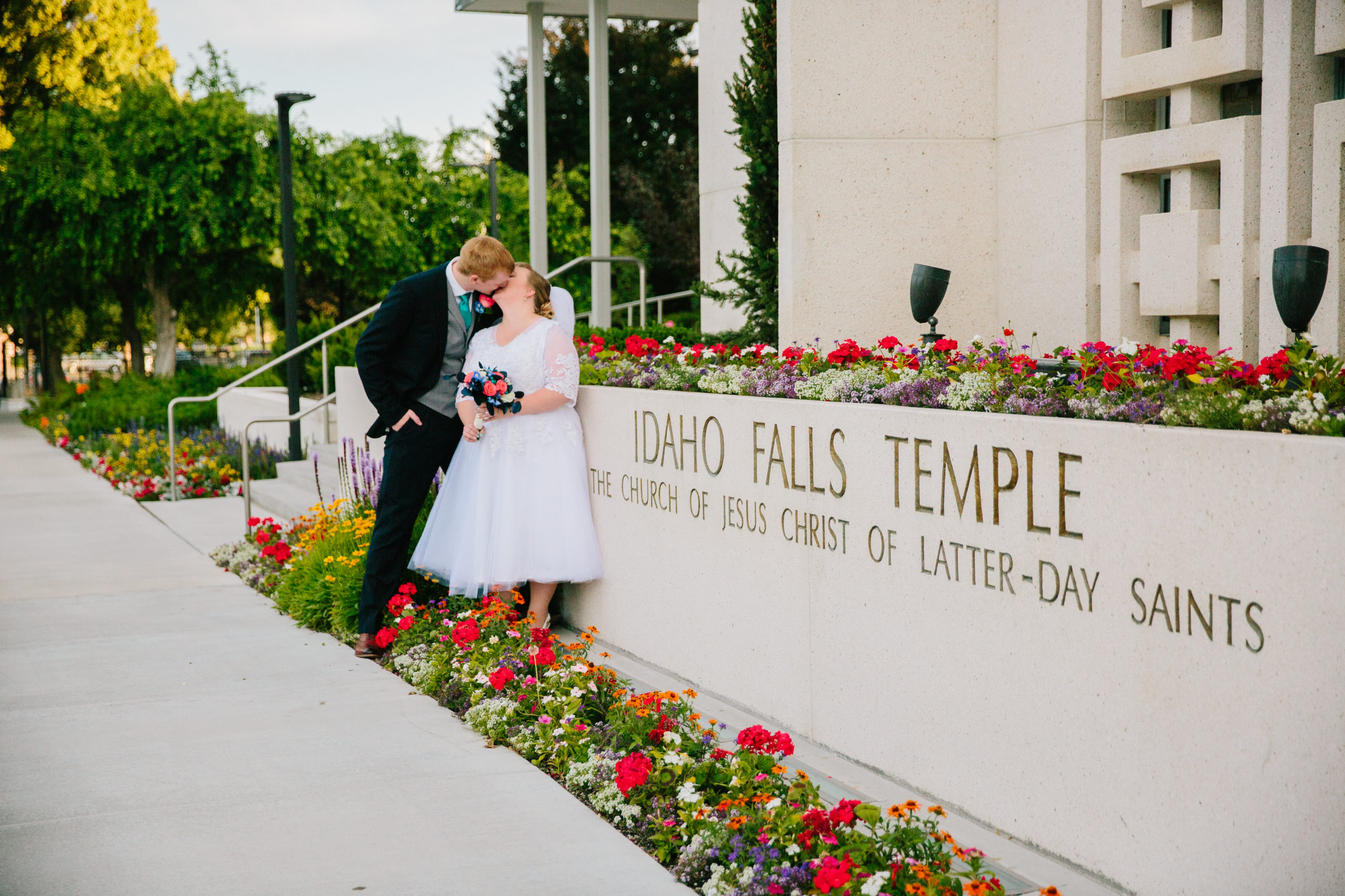 bride and groom standing outside of Idaho Falls temple in red flowers