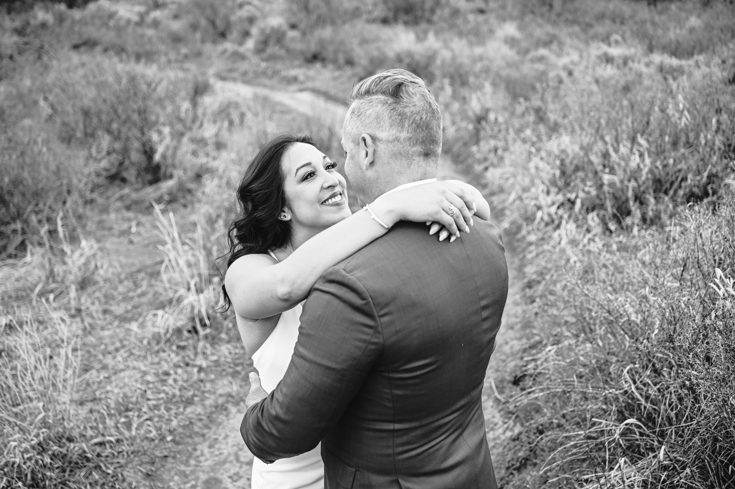 bride holding her groom around the shoulders as he embraces her at the waist for thier outdoor Pocatello wedding photos