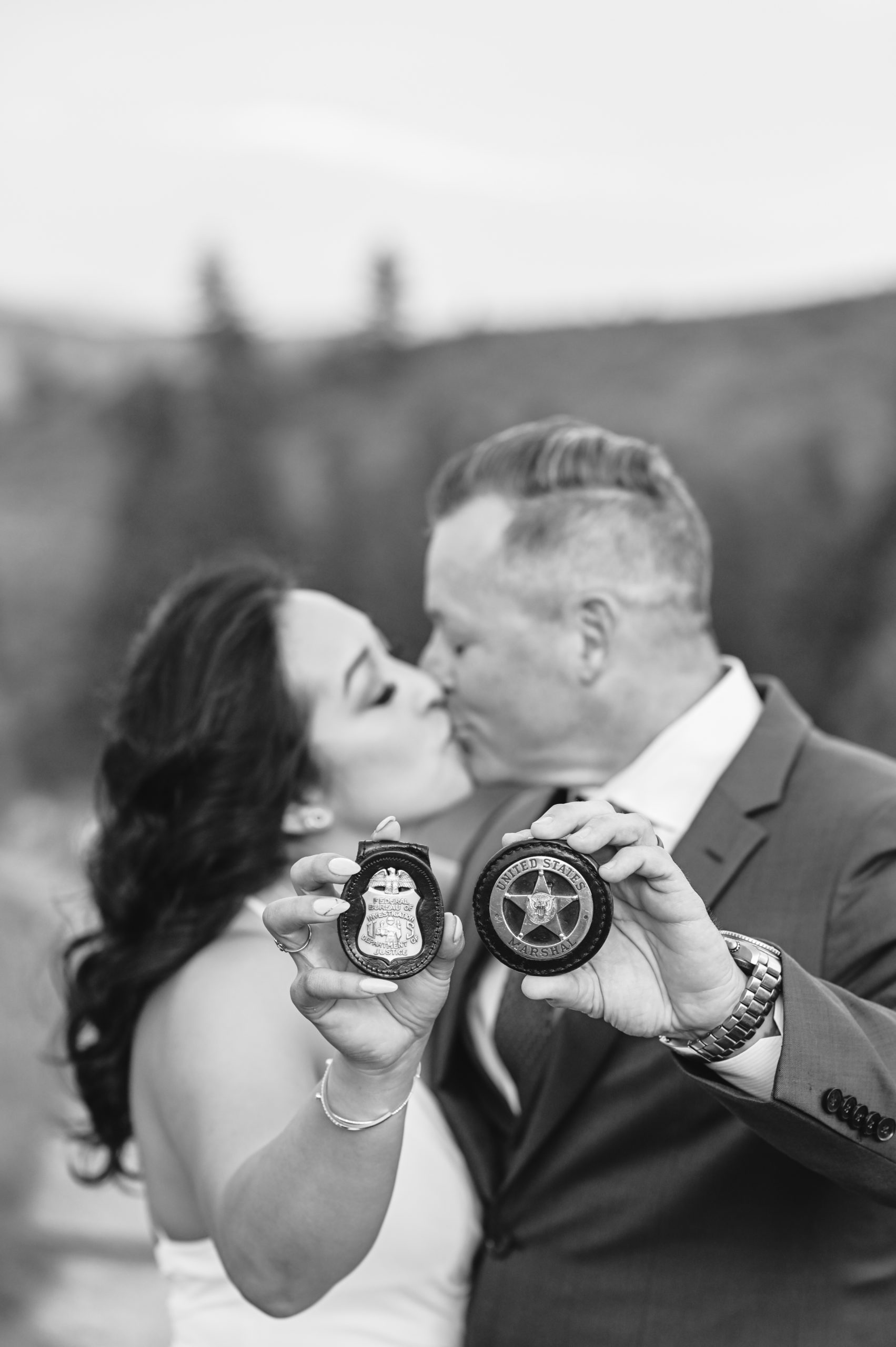 bride and groom kissing as they hold up their police badges to the camera