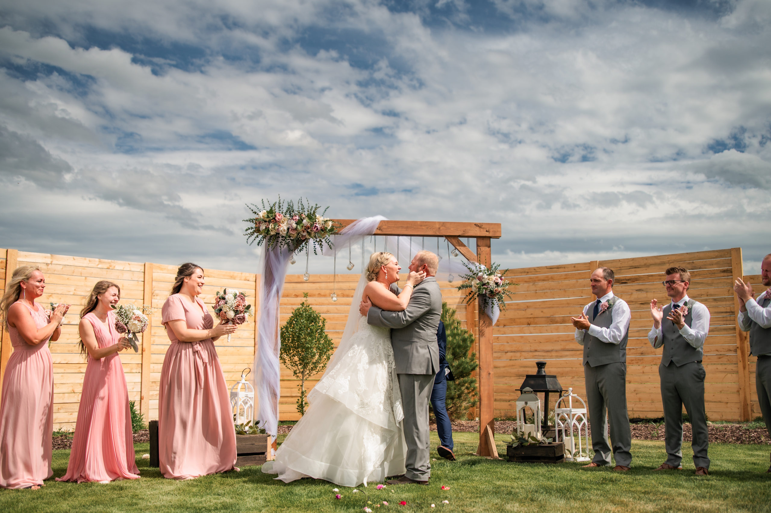 bride and groom kissing under their wedding arbor with their bridal party surrounding them on their Pocatello wedding day 