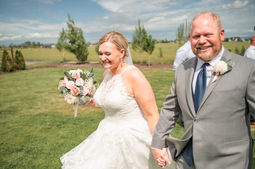 bride and groom holding hands as they walk through their Pocatello wedding venue for their outdoor summer wedding in Pocatello