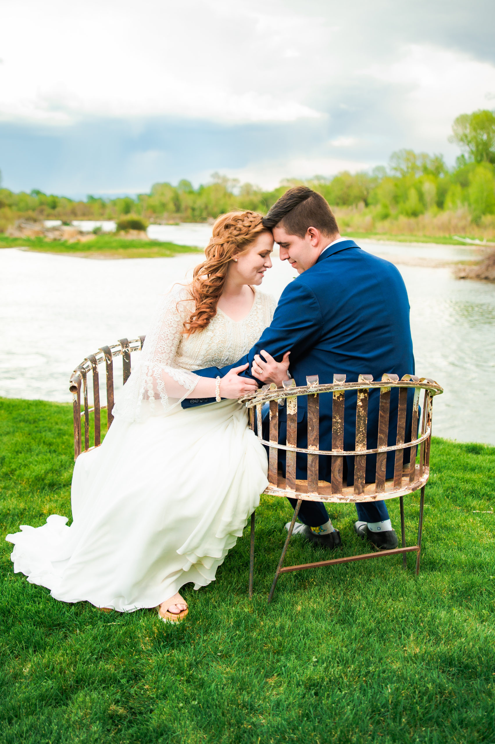 bride and groom sitting on bench next to river
