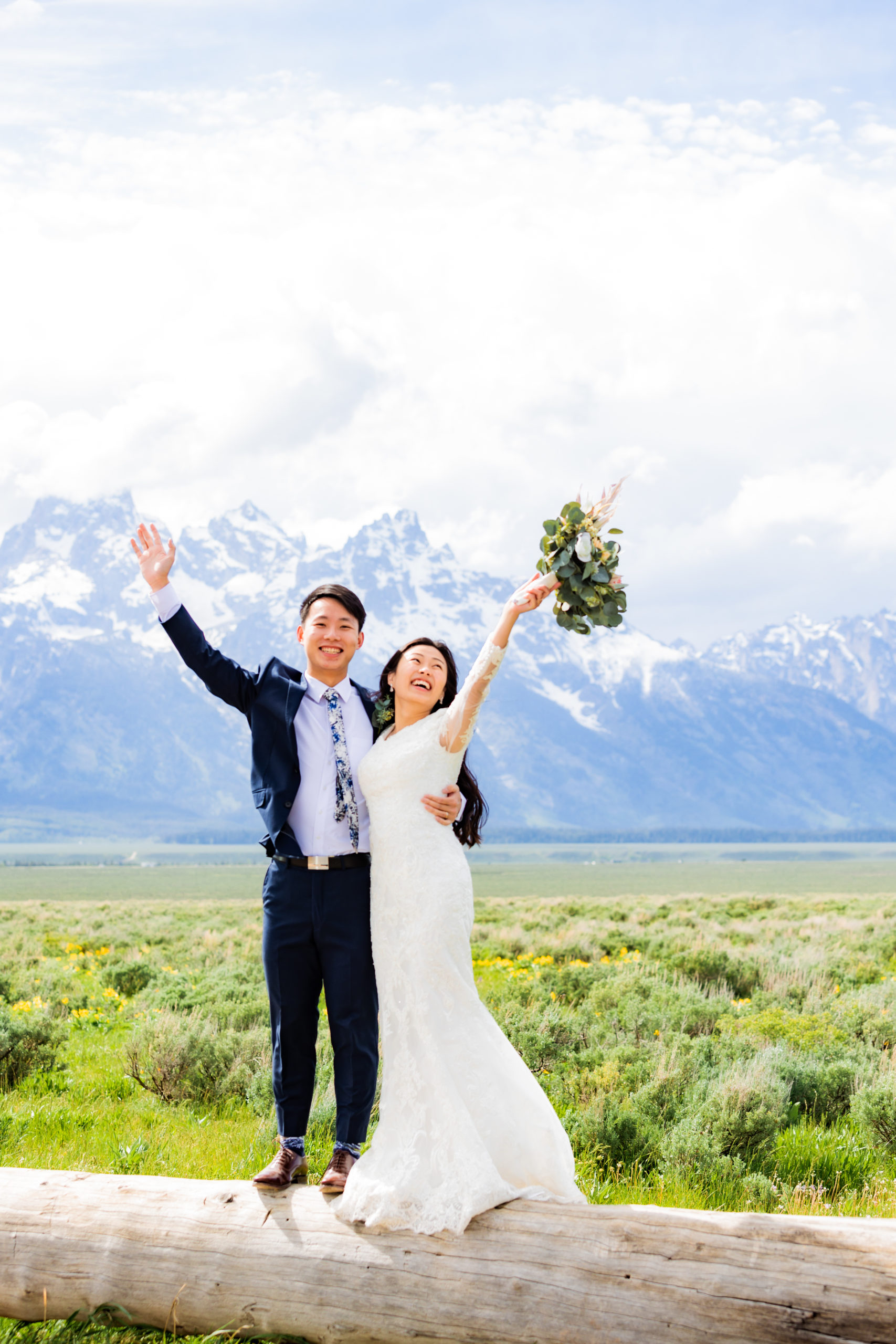 bride and groom hold their arms up in the air together as they celebrate their wedding day in the Tetons