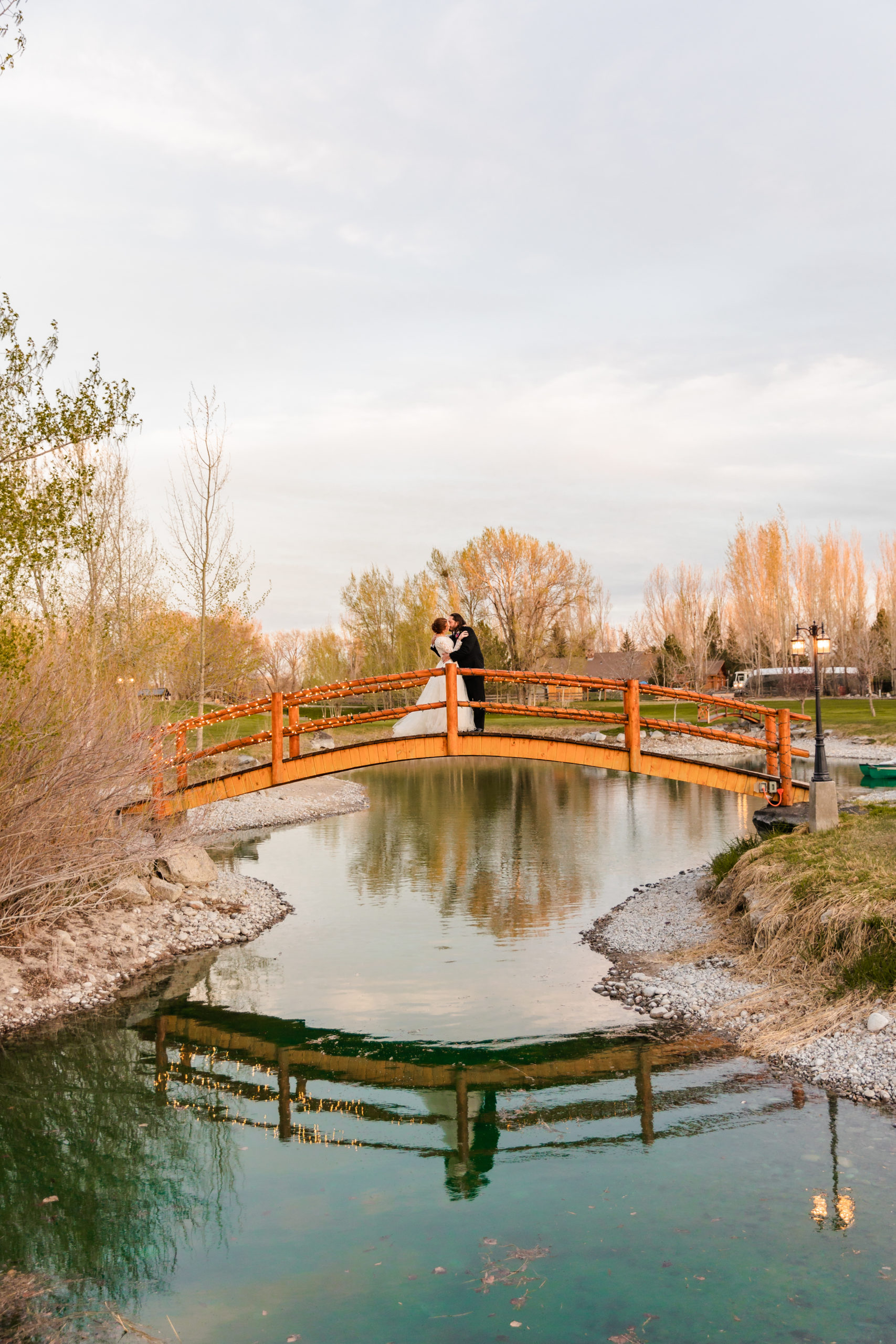 bride and groom standing on bridge kissing during outdoor portraits