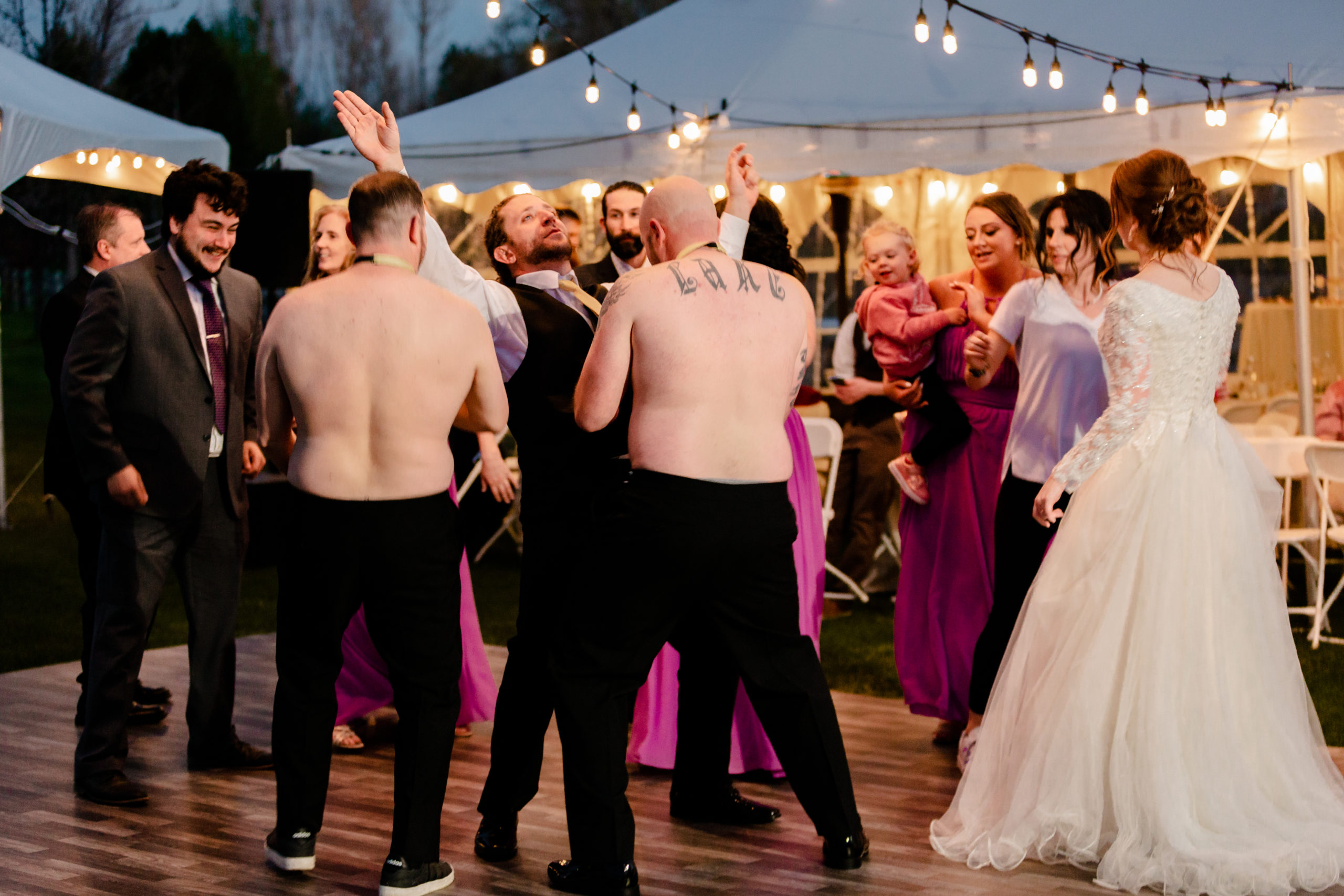 wedding guests with shirts off dancing at sunset