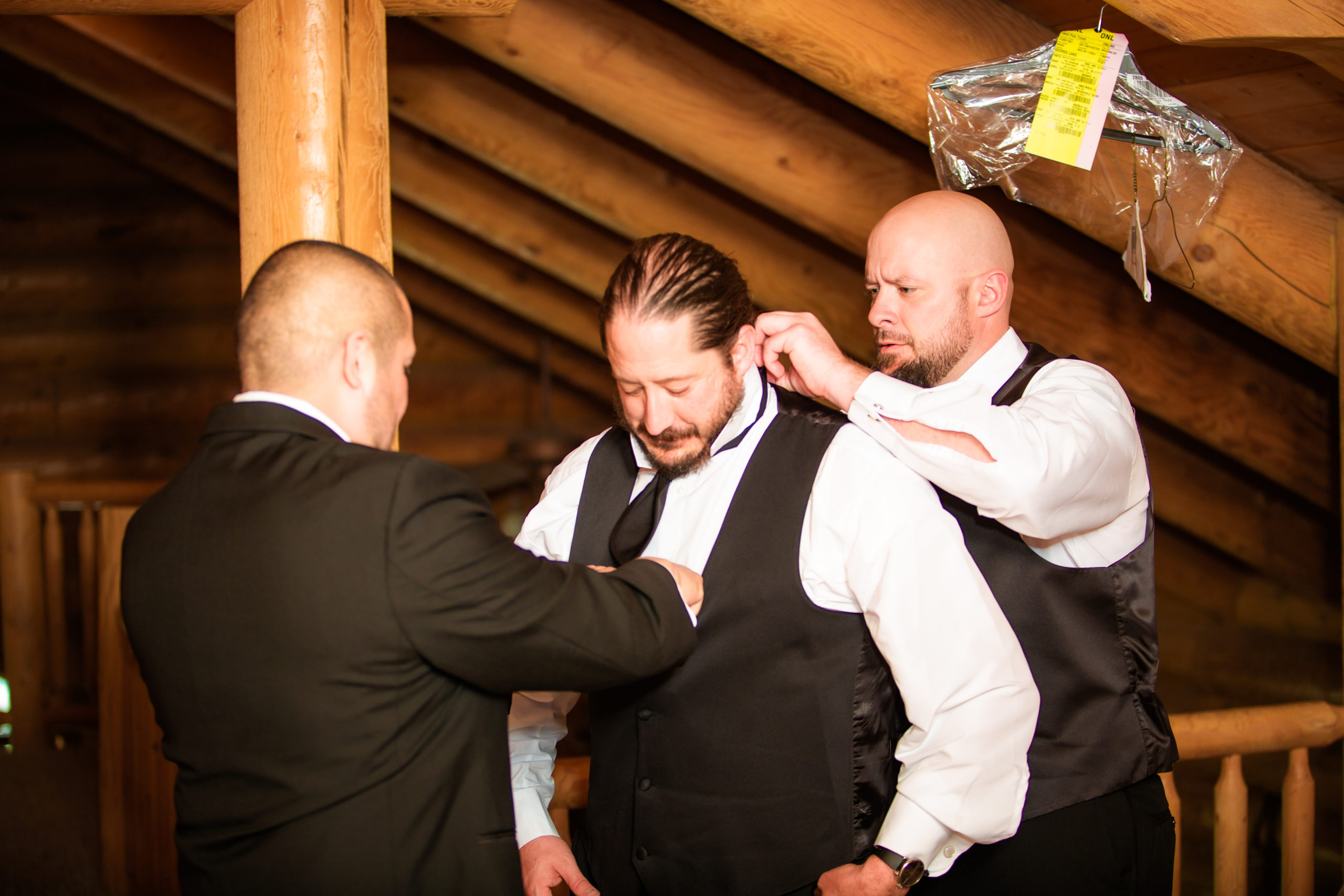 groomsmen helping groom into his tux before wedding at labelle lake idaho wedding venue