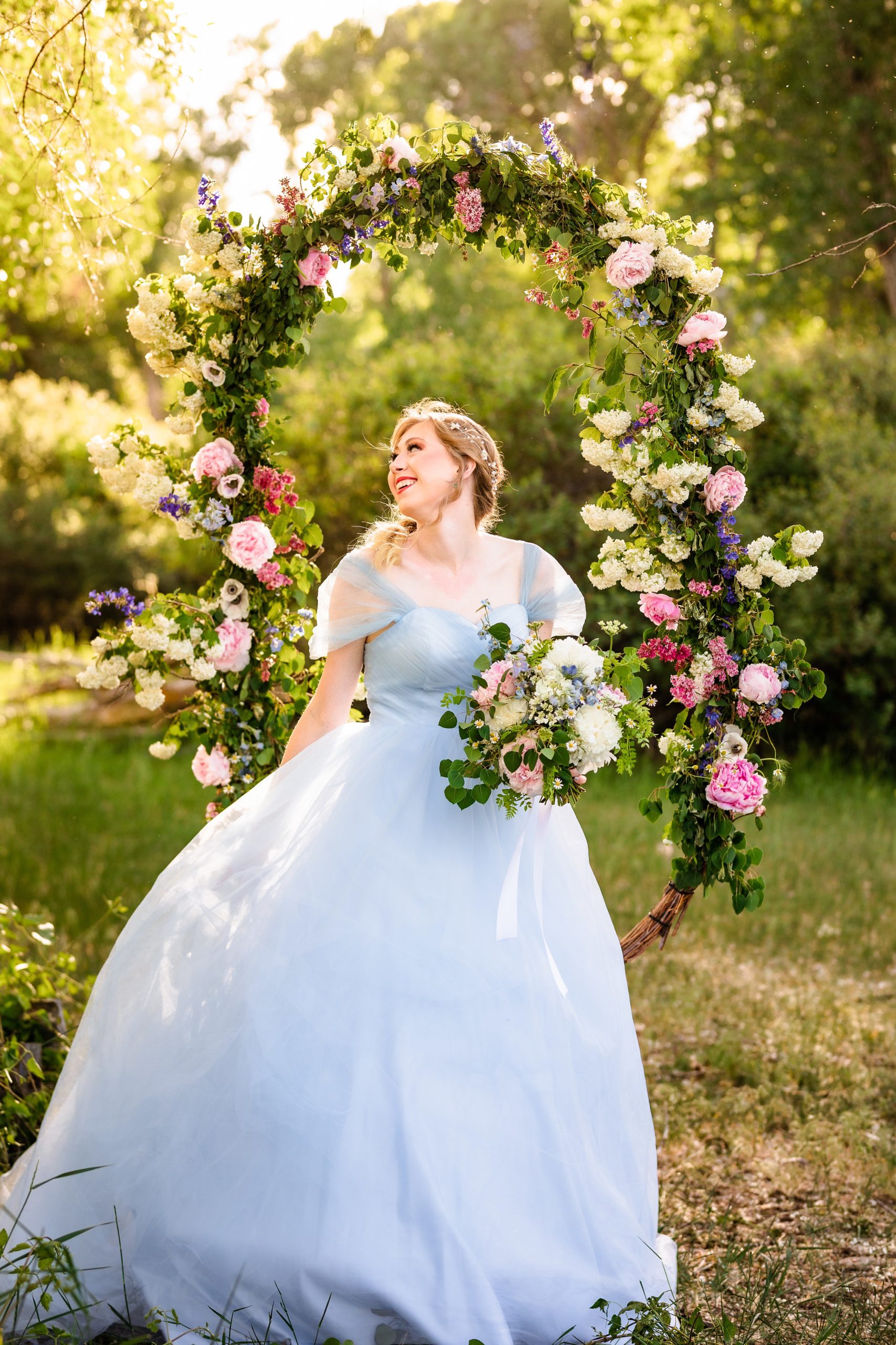 bride in blue dress in front of swing covered in pink flowers laughs