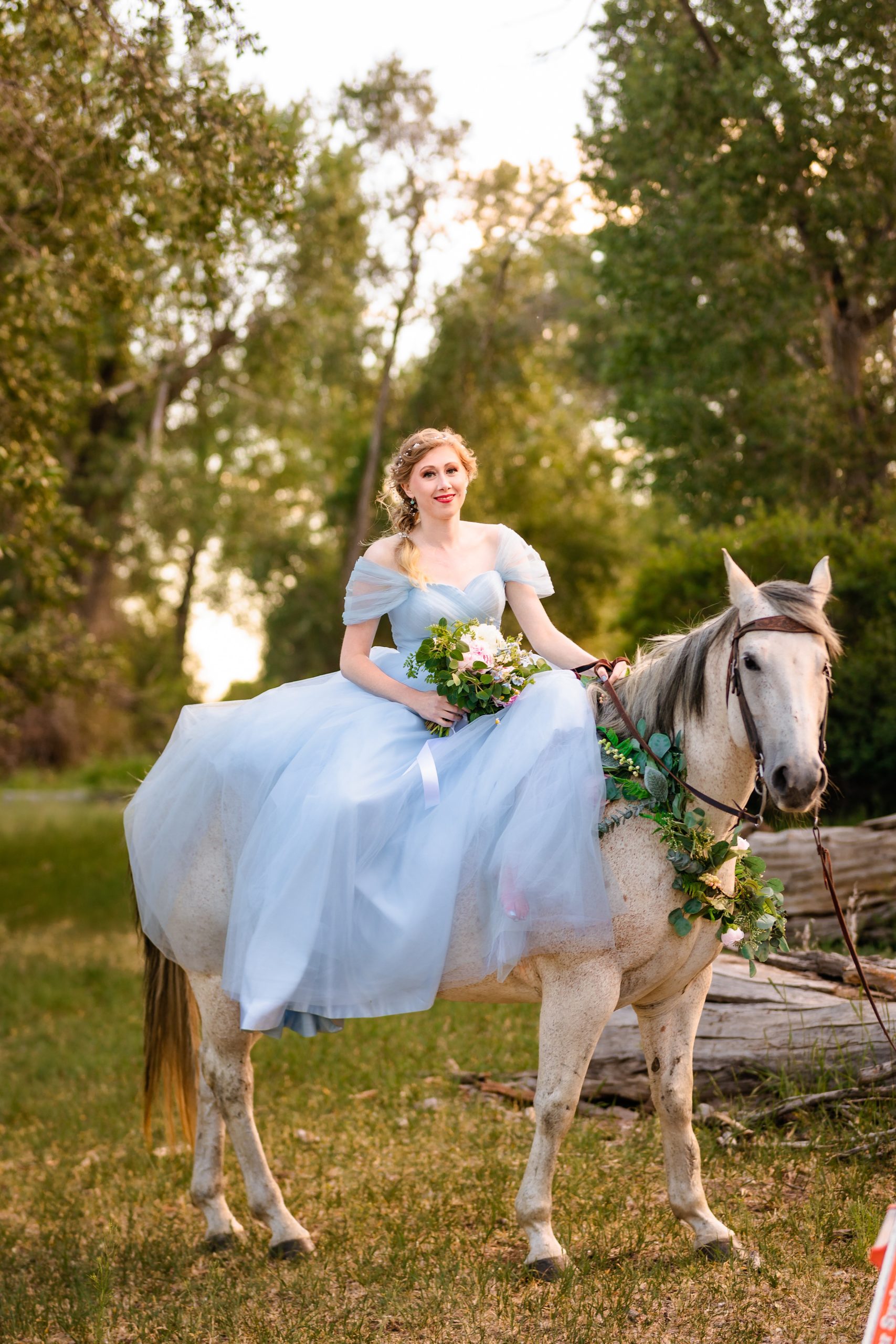 bride in blue horse sits on top of white horse in forest