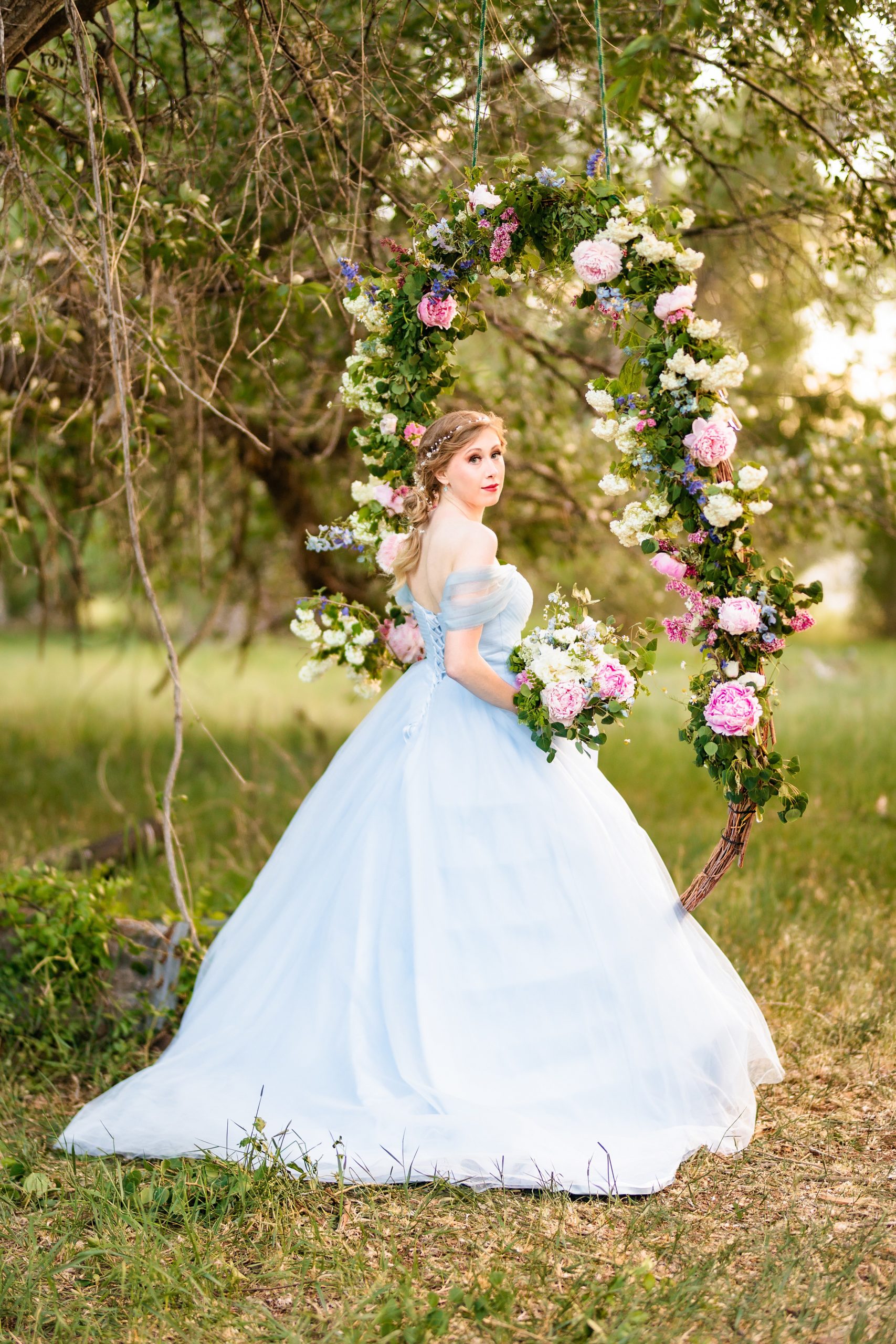 swing with pink flowers while bride in blue dress gazes behind
