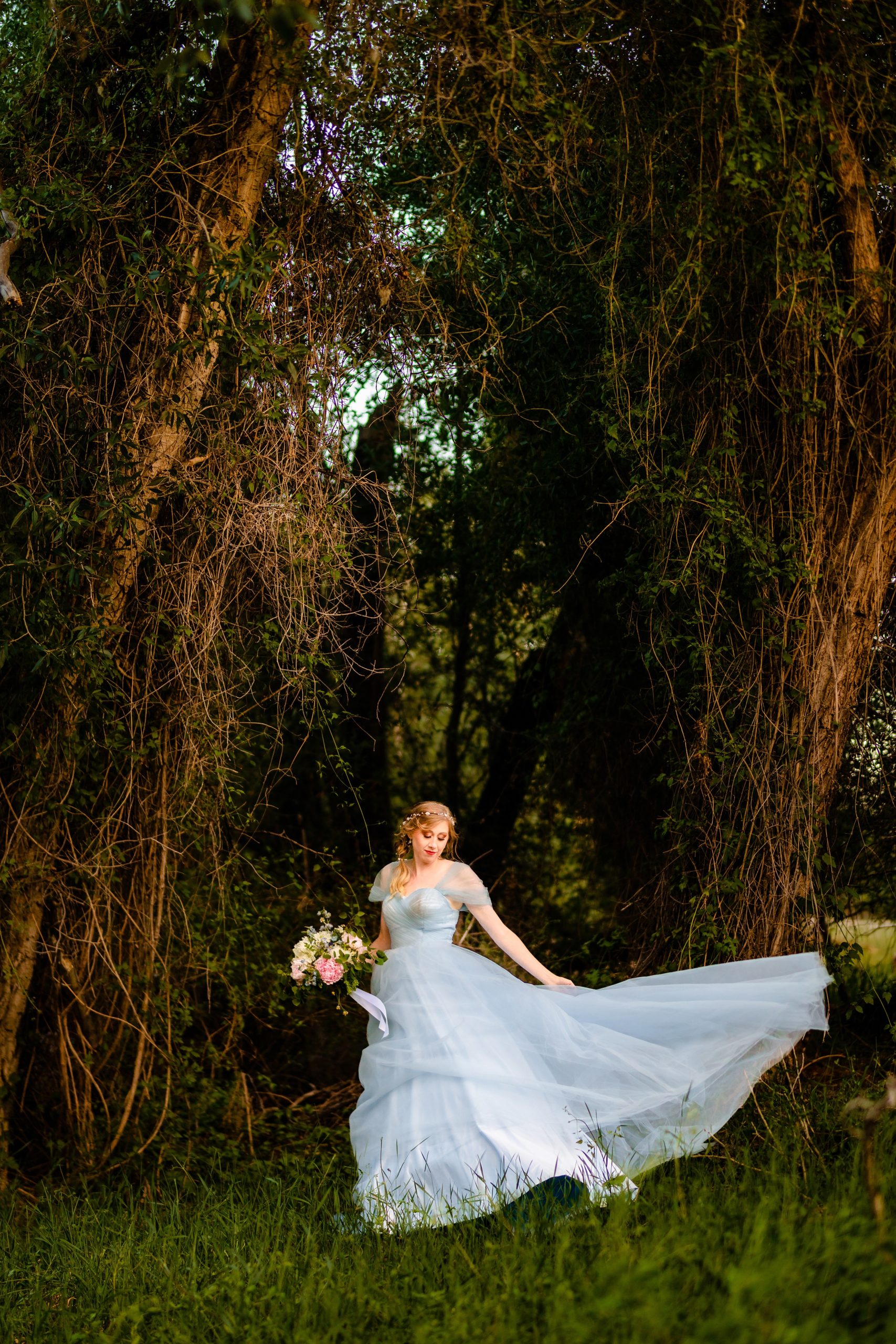 windy bride in blue dress standing along in forest with wind blowing dress