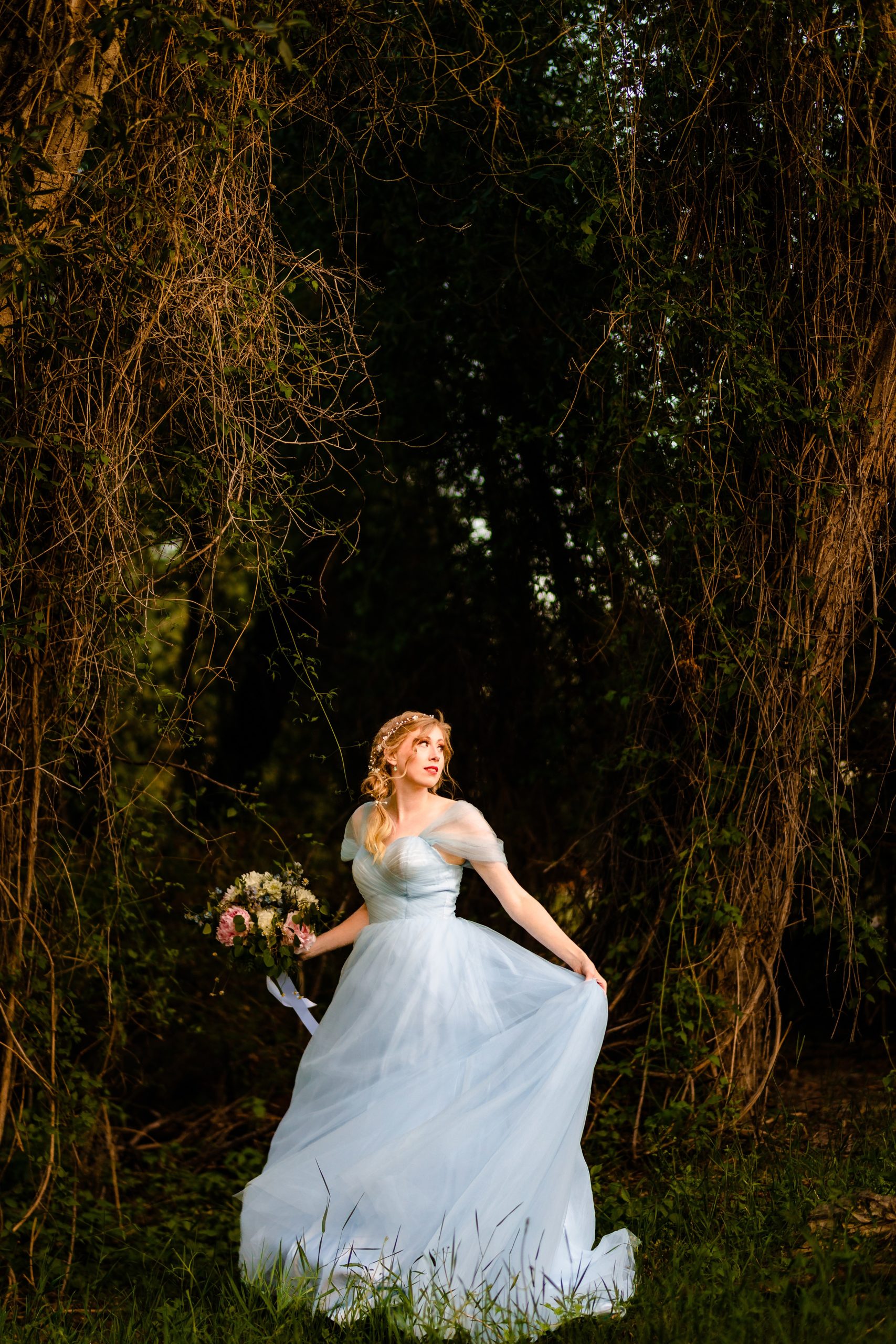 elopement-bride in blue dress standing along in forest with wind blowing dress