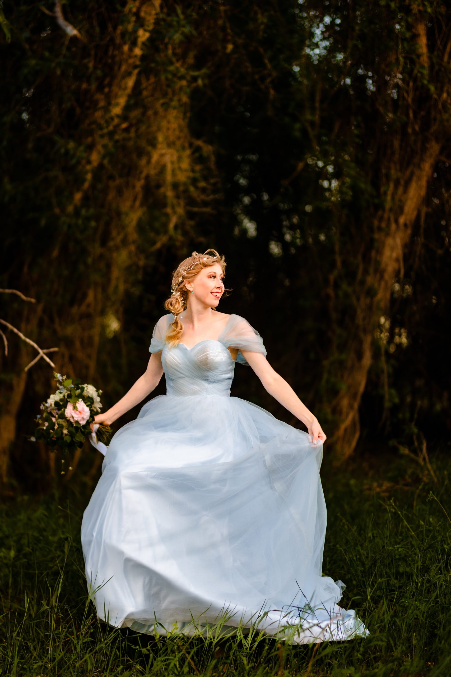 whimsical bride in blue dress standing along in forest with wind blowing dress