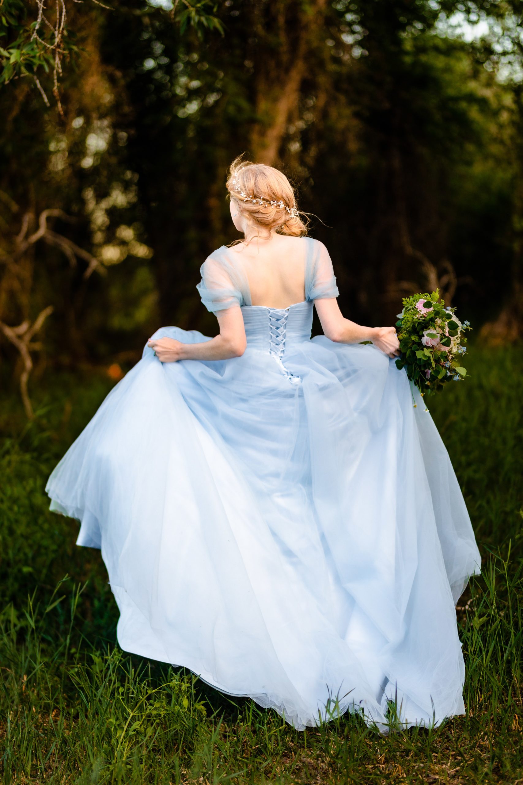 running away bride in blue dress standing along in forest with wind blowing dress