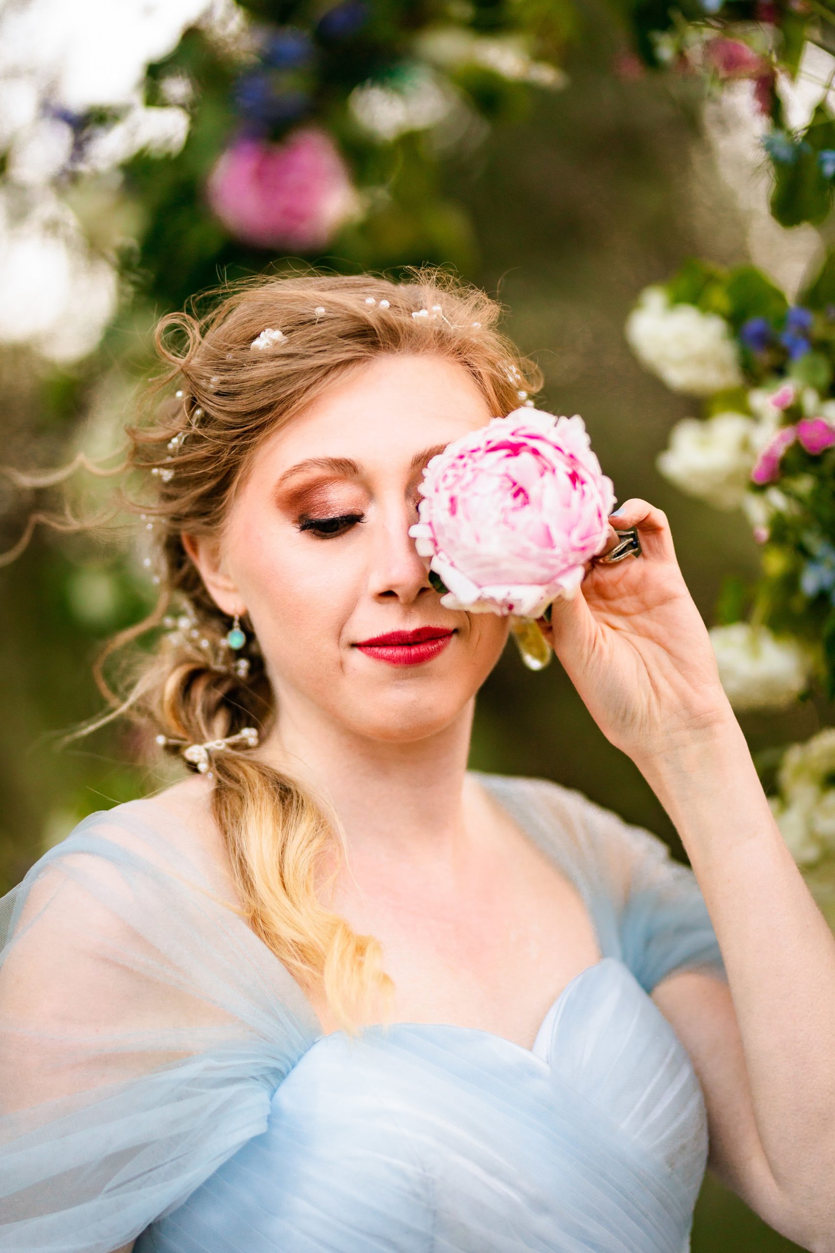 bride in blue dress holds pink peony near eye