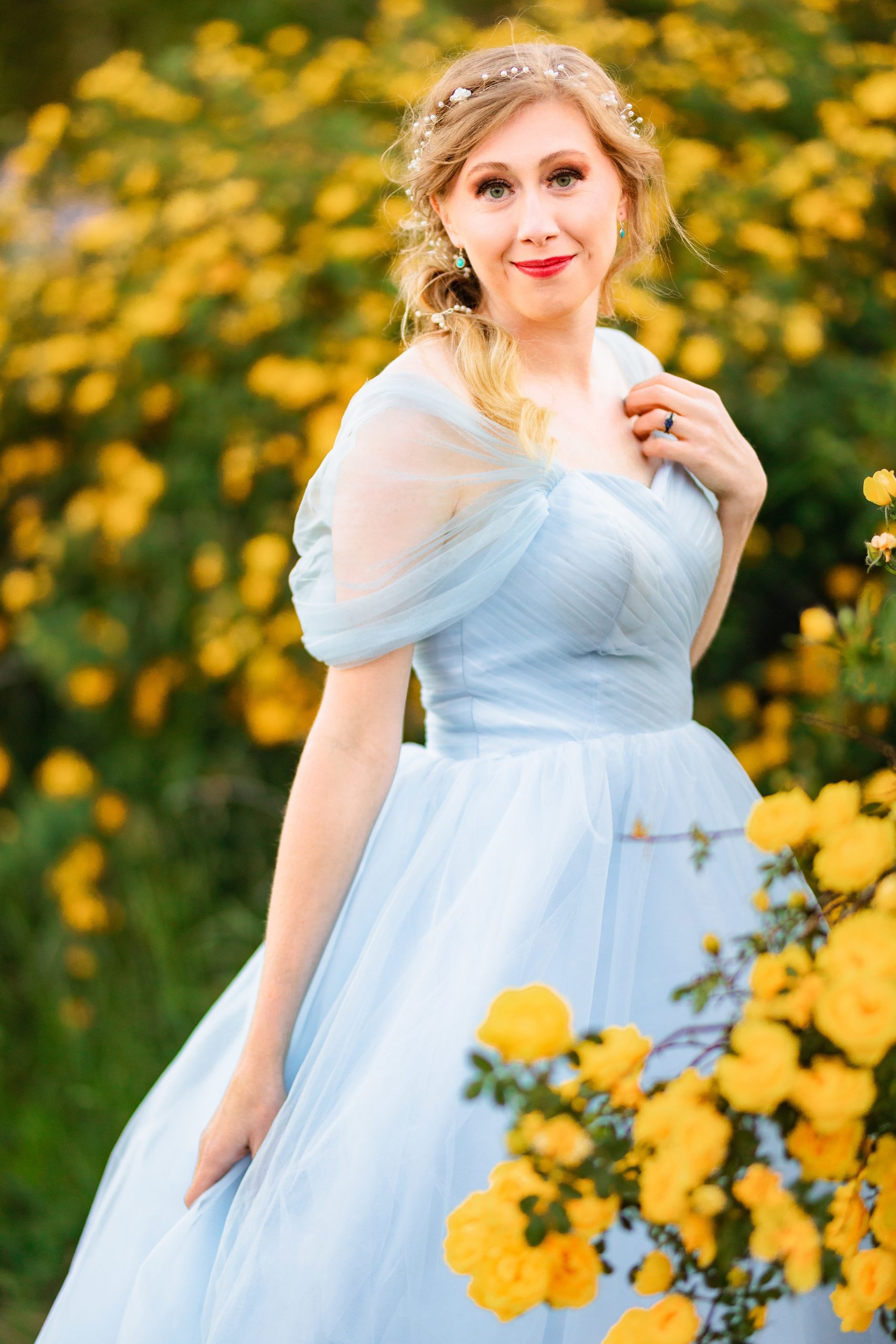 bride in blue dress in yellow rose bush looks at camera