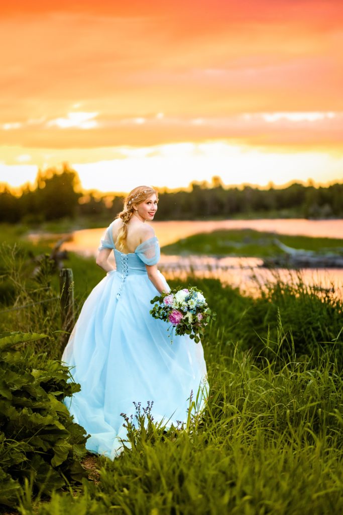 smiling bride in blue dress with orange and pink sunset next to beautiful river