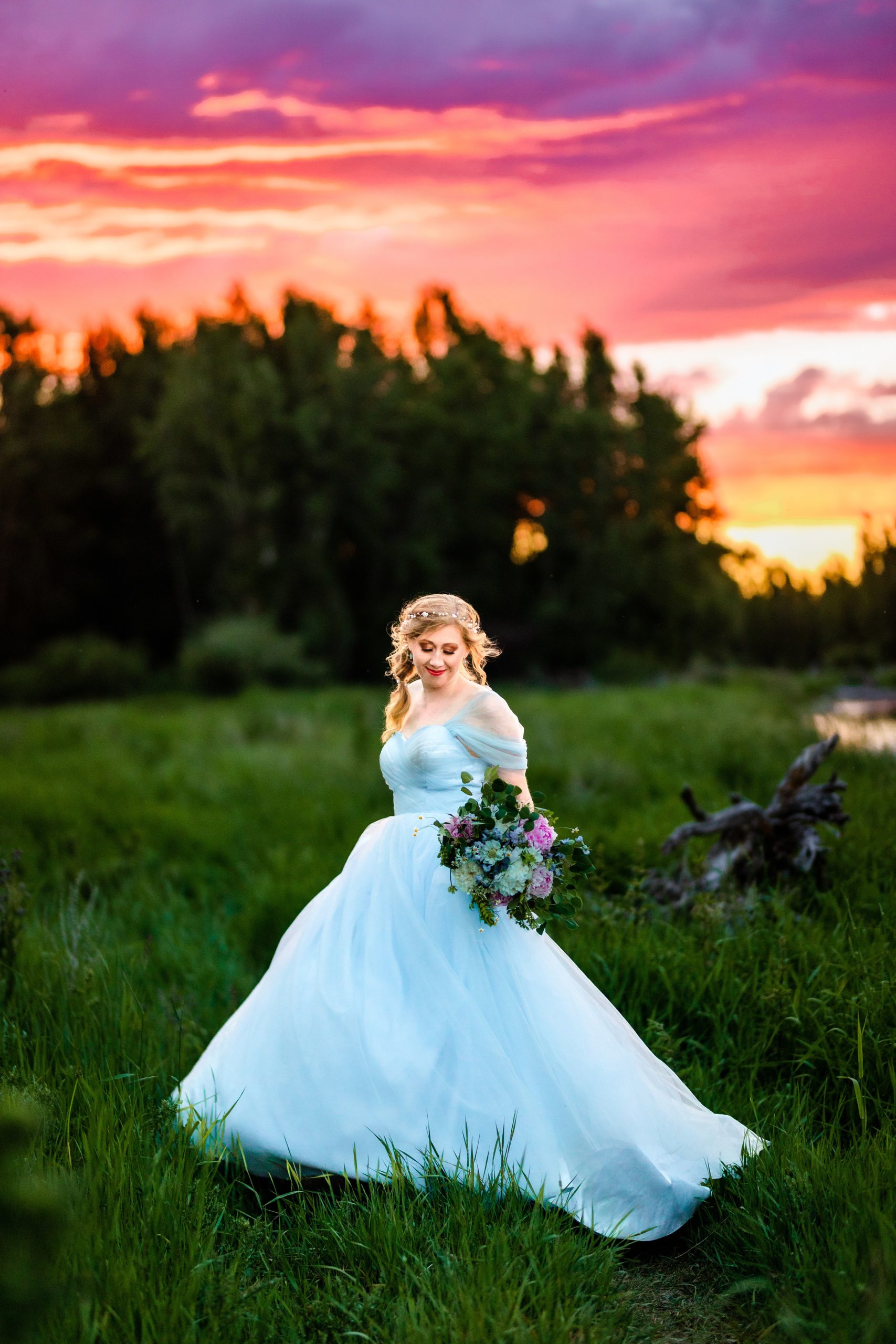 colorful forest bride in blue dress with orange and pink sunset next to beautiful river