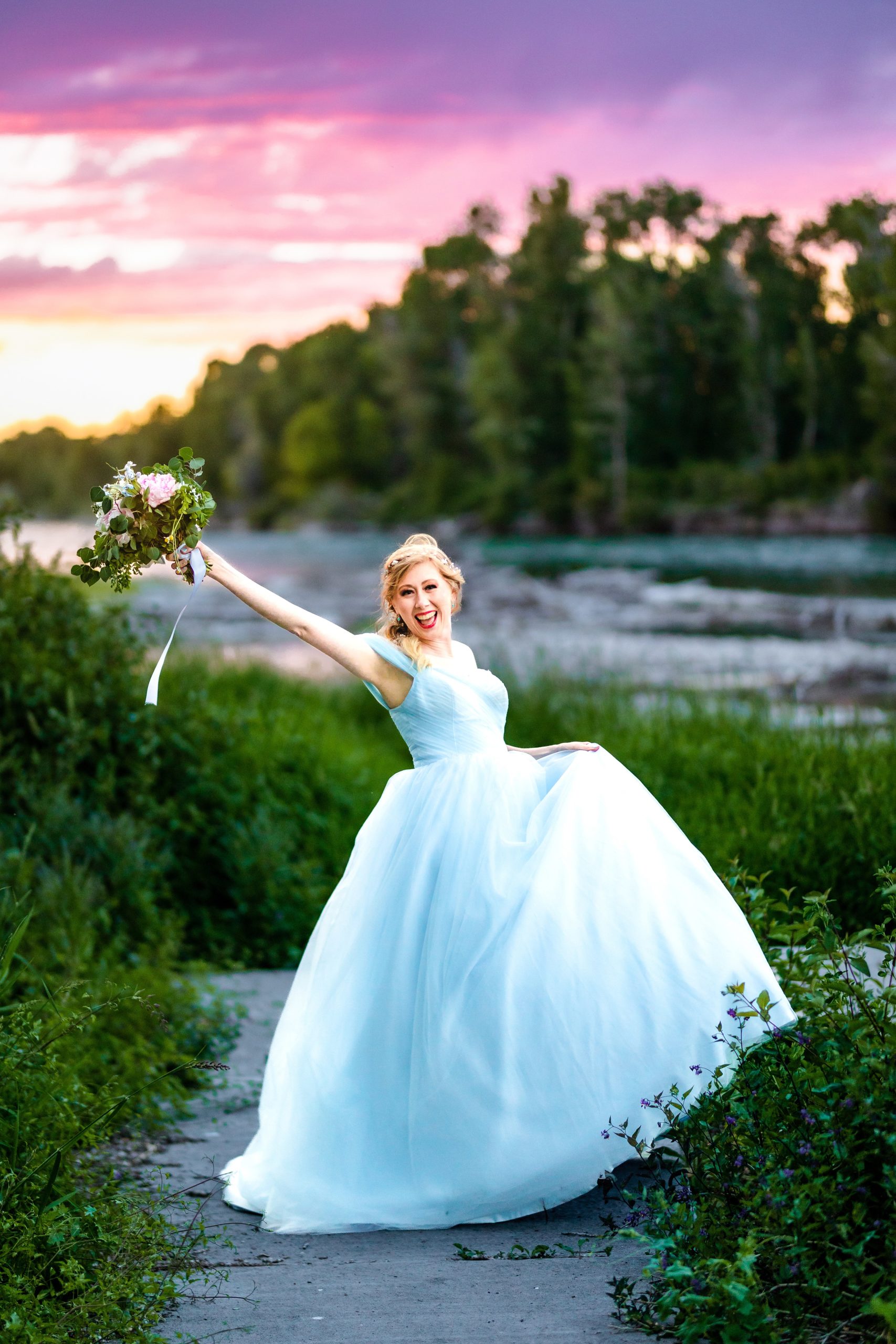 bride in blue dress with orange and pink sunset next to beautiful river celebrates