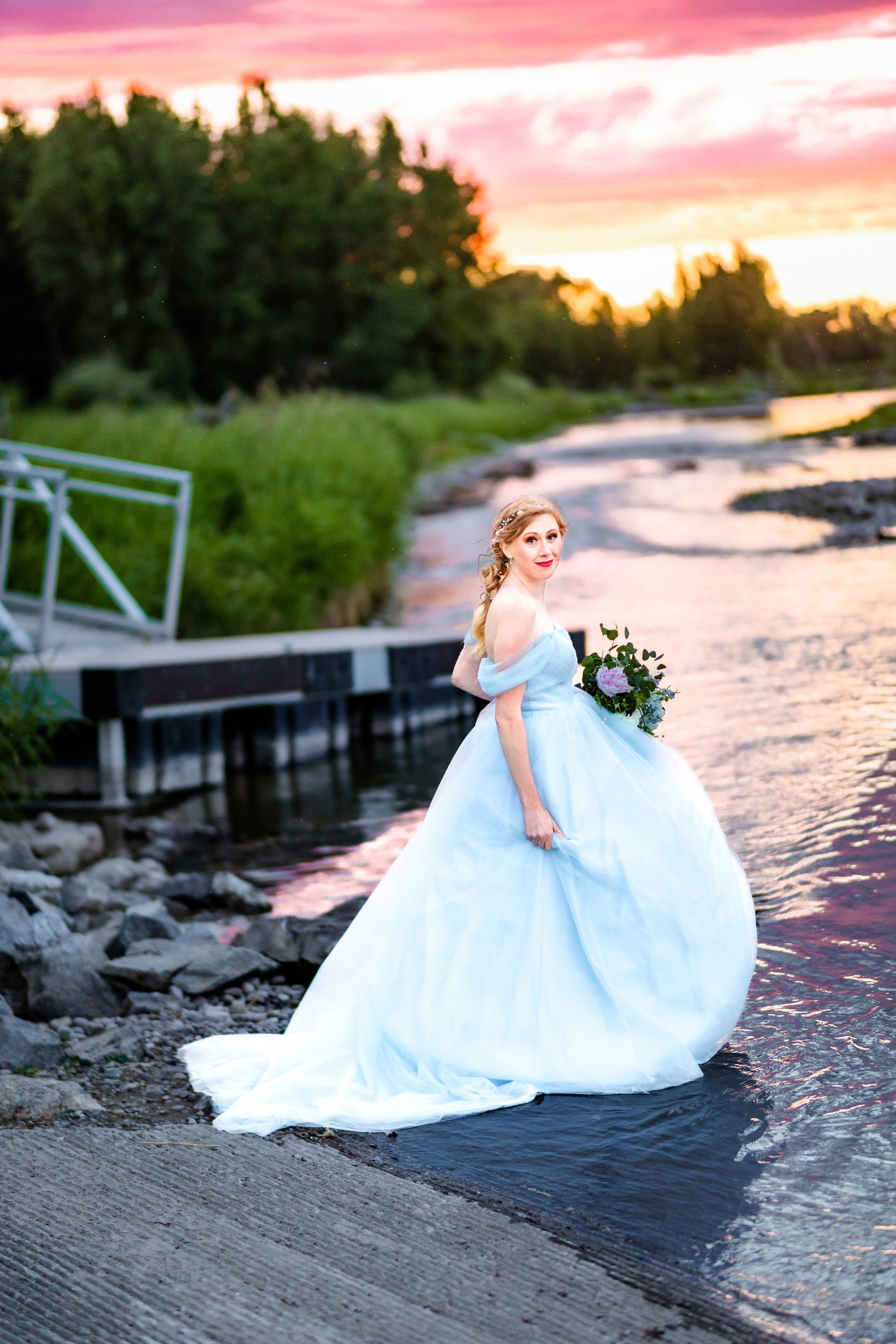 boat-dock-bride in blue dress with orange and pink sunset next to beautiful river